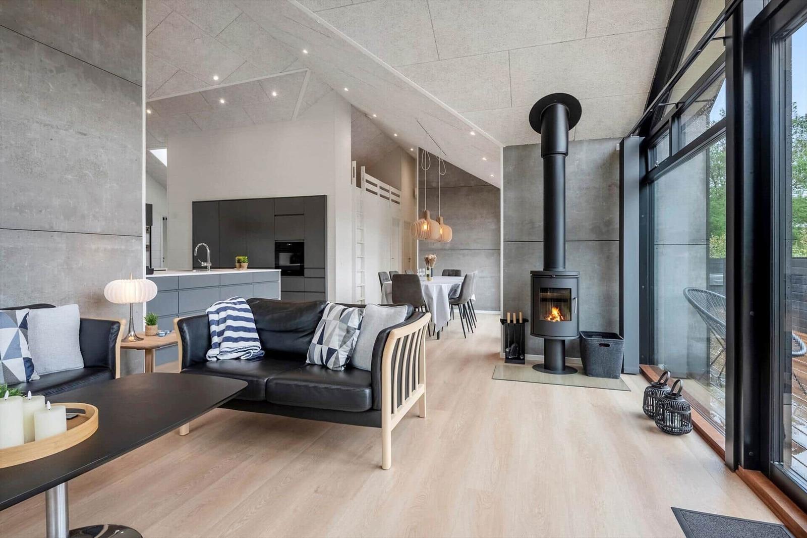 Wohnbereich mit Sofa, Kamin und Essbereich. Große Fenster und helles Holzfußboden.