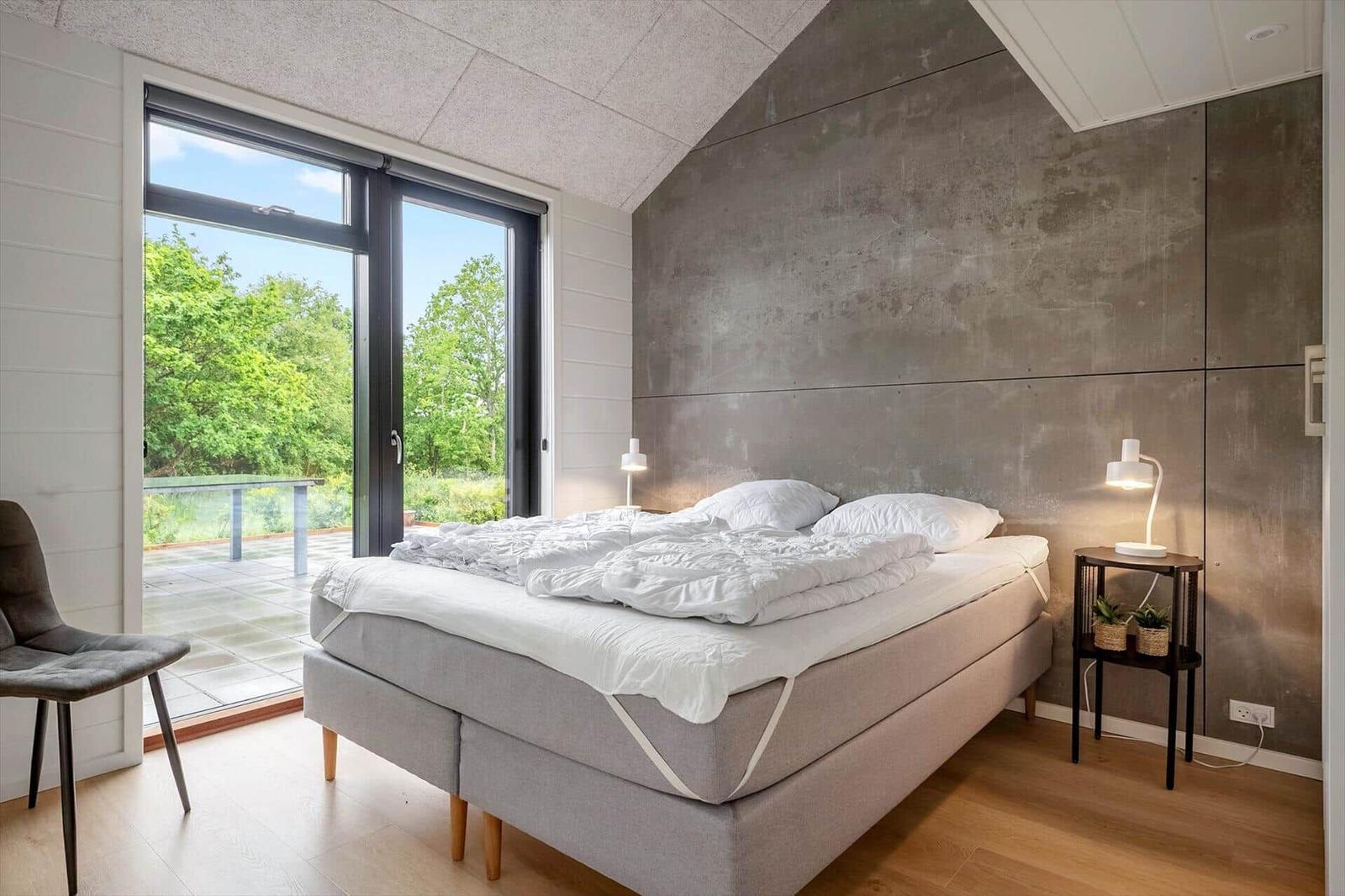 Schlafzimmer mit Bett, Nachttisch und Fenster zur Terrasse.