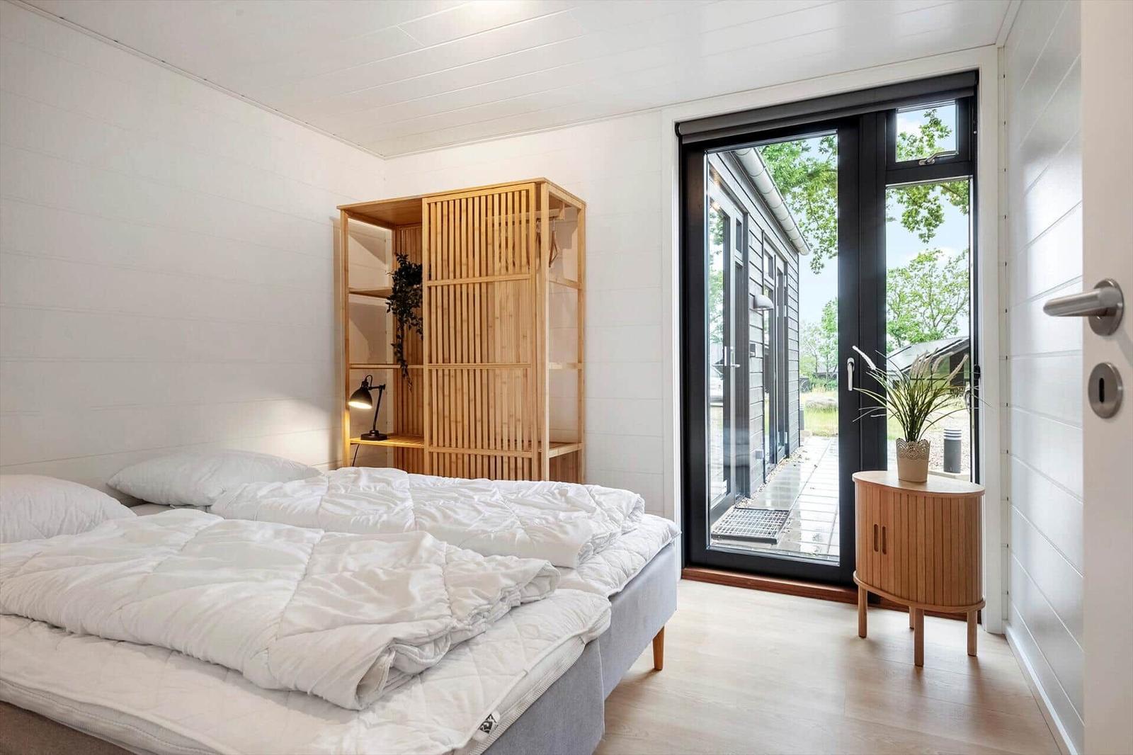 Schlafzimmer mit Bett, Holzregal und Glasfront zur Außenterrasse.