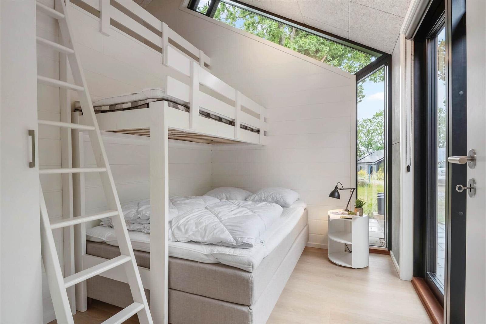 Schlafzimmer mit Doppelbett und Oberbett. Große Fensterfront mit Blick auf Garten.