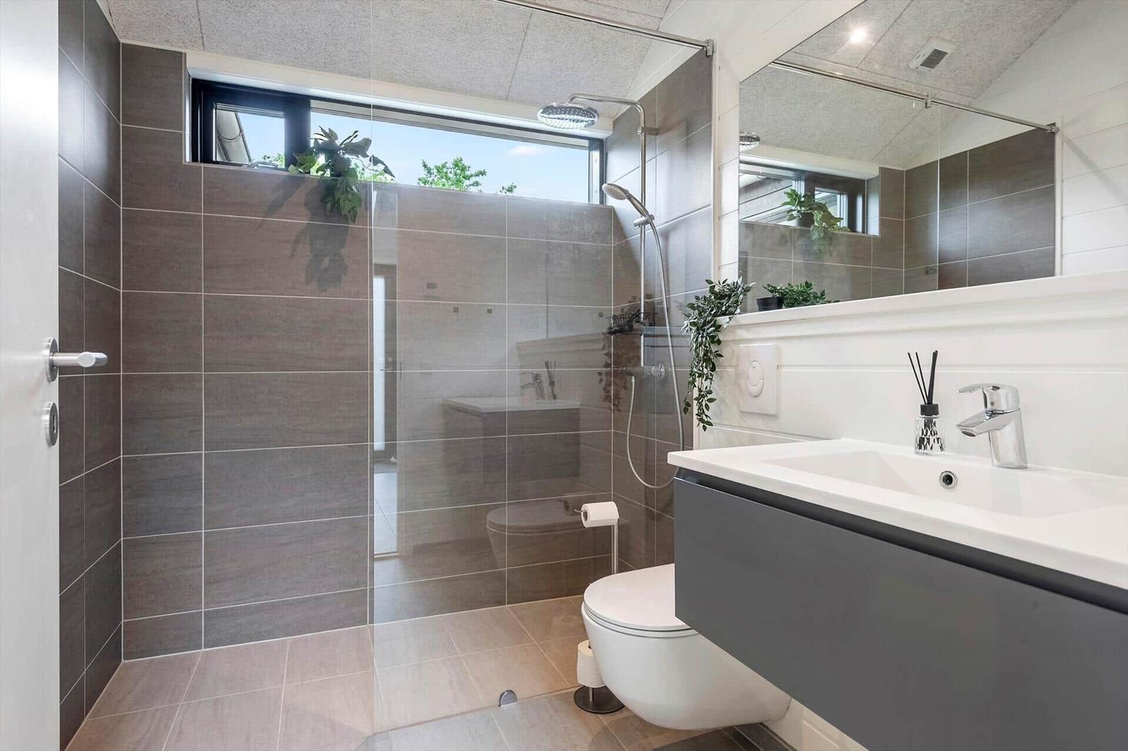 Moderne Badezimmer mit Dusche, Waschbecken und Toilette. Große Fensterfront mit Blick auf Grün.