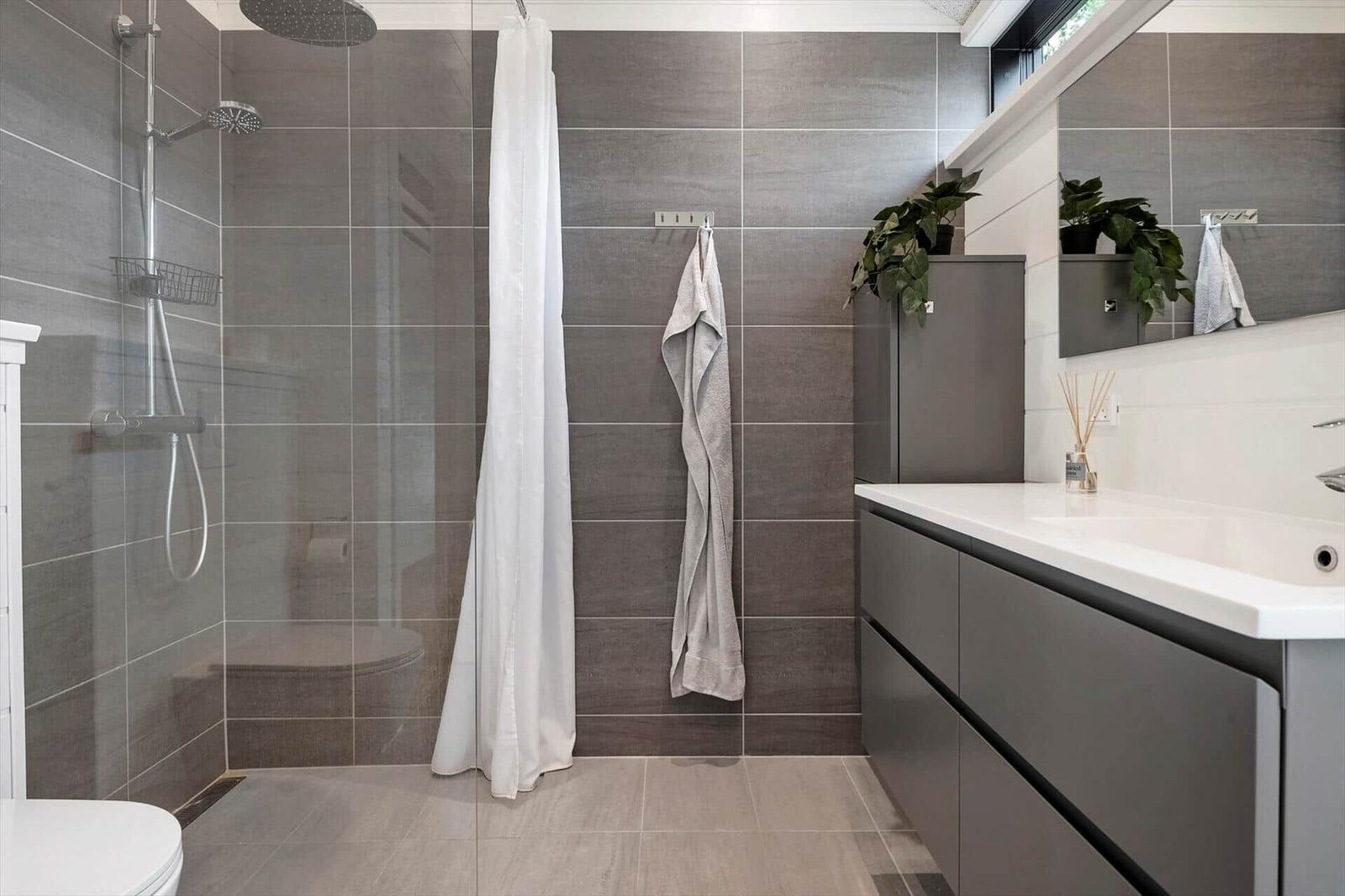 Dusche mit Duschvorhang, Waschbecken und Pflanze im Badezimmer