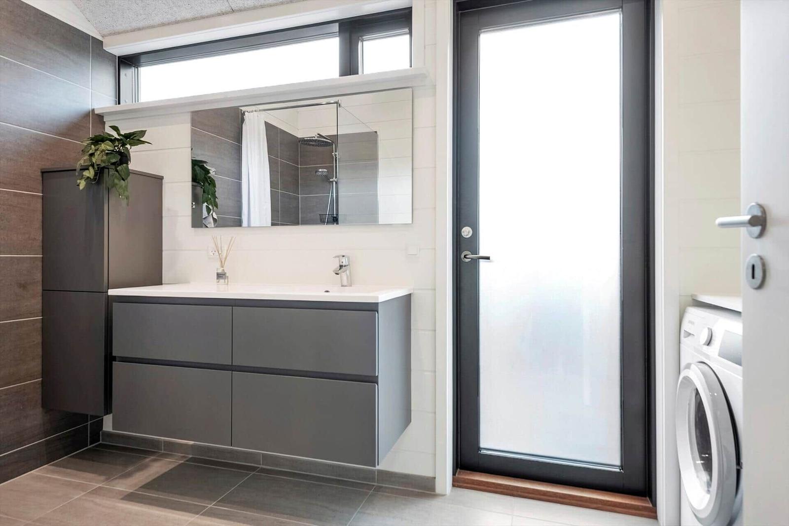 Moderne Badezimmer mit Waschbecken, Spiegel und Dusche. Tür und Waschmaschine sind sichtbar.
