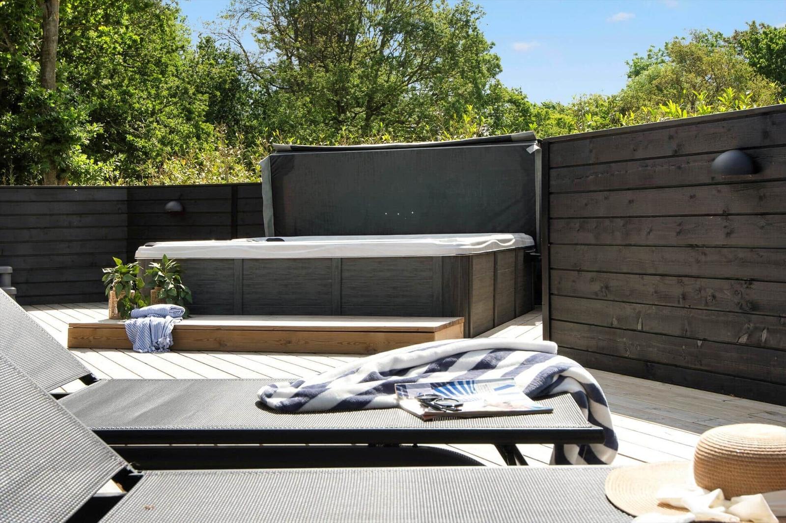 Terrasse mit Whirlpool, Liegen und Pflanzen. Holzwand und Sonnenschutz sichtbar.