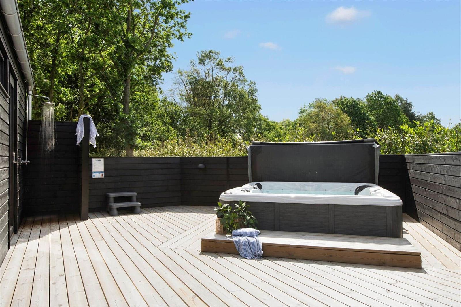 Terrasse mit Whirlpool und Duschbereich umgeben von Bäumen.