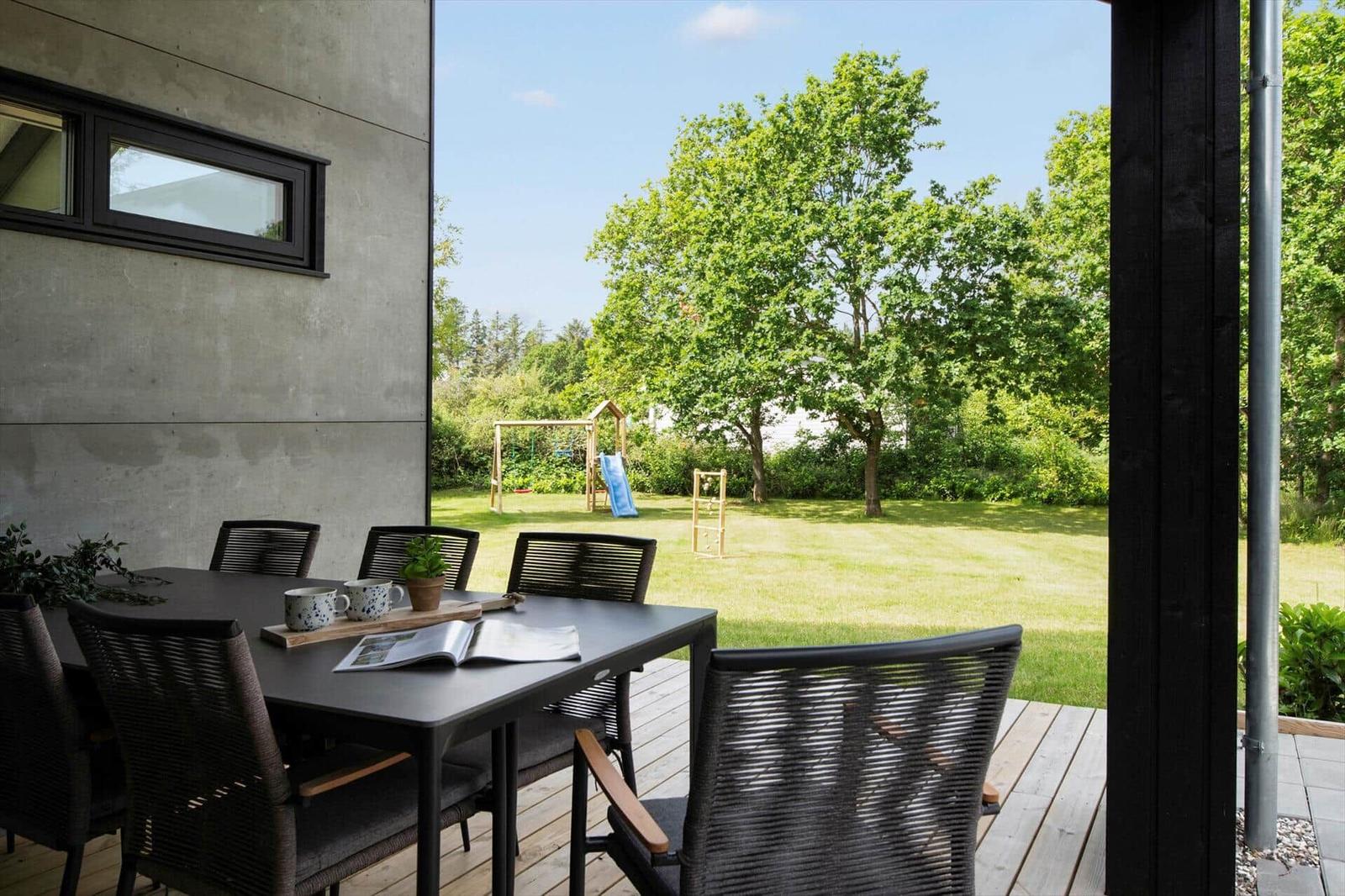Terrasse mit Tisch und Stühlen, Blick auf grünen Garten mit Spielplatz.