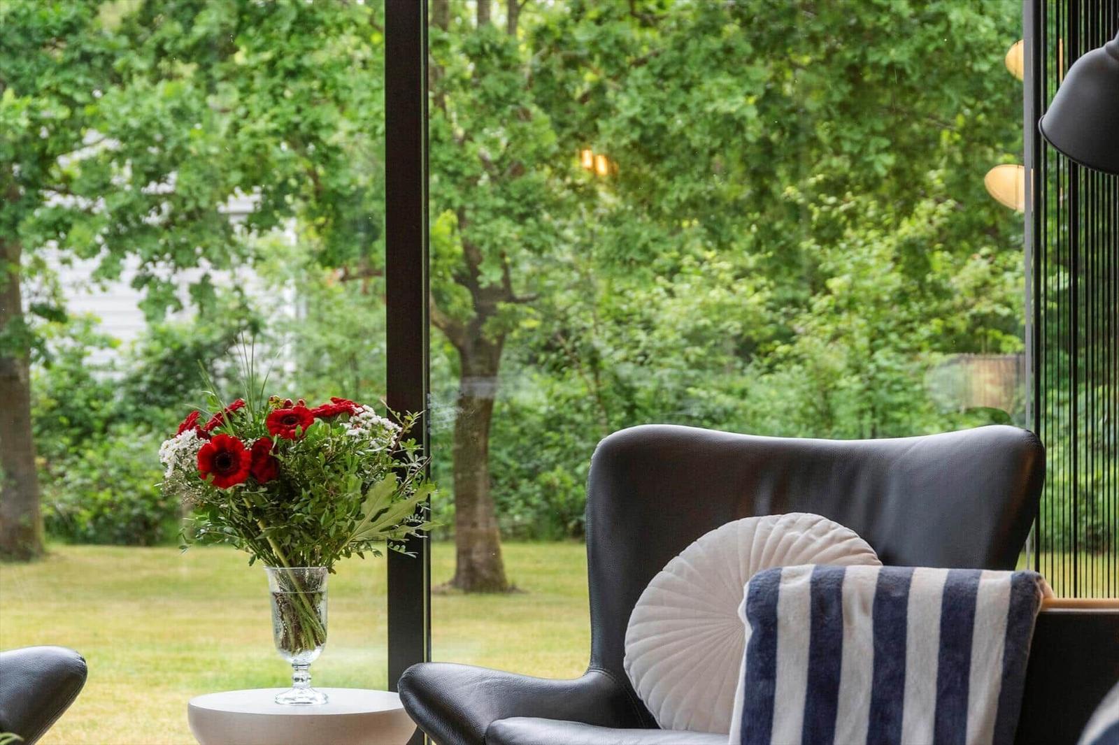 Ein dunkler Sessel mit Kissen und einem Blumenstrauß vor einem großen Fenster.