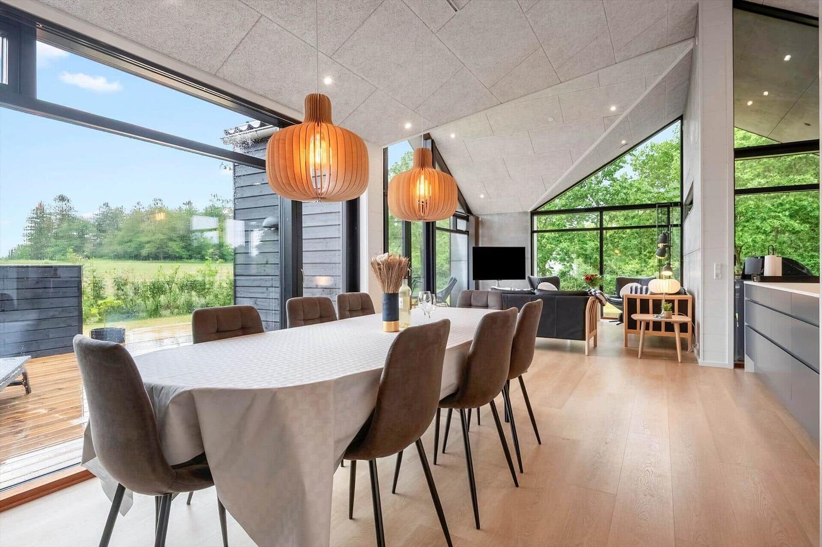 Essbereich mit Tisch, Stühlen und großen Fenstern. Wohnbereich mit Sofa und Fernseher.