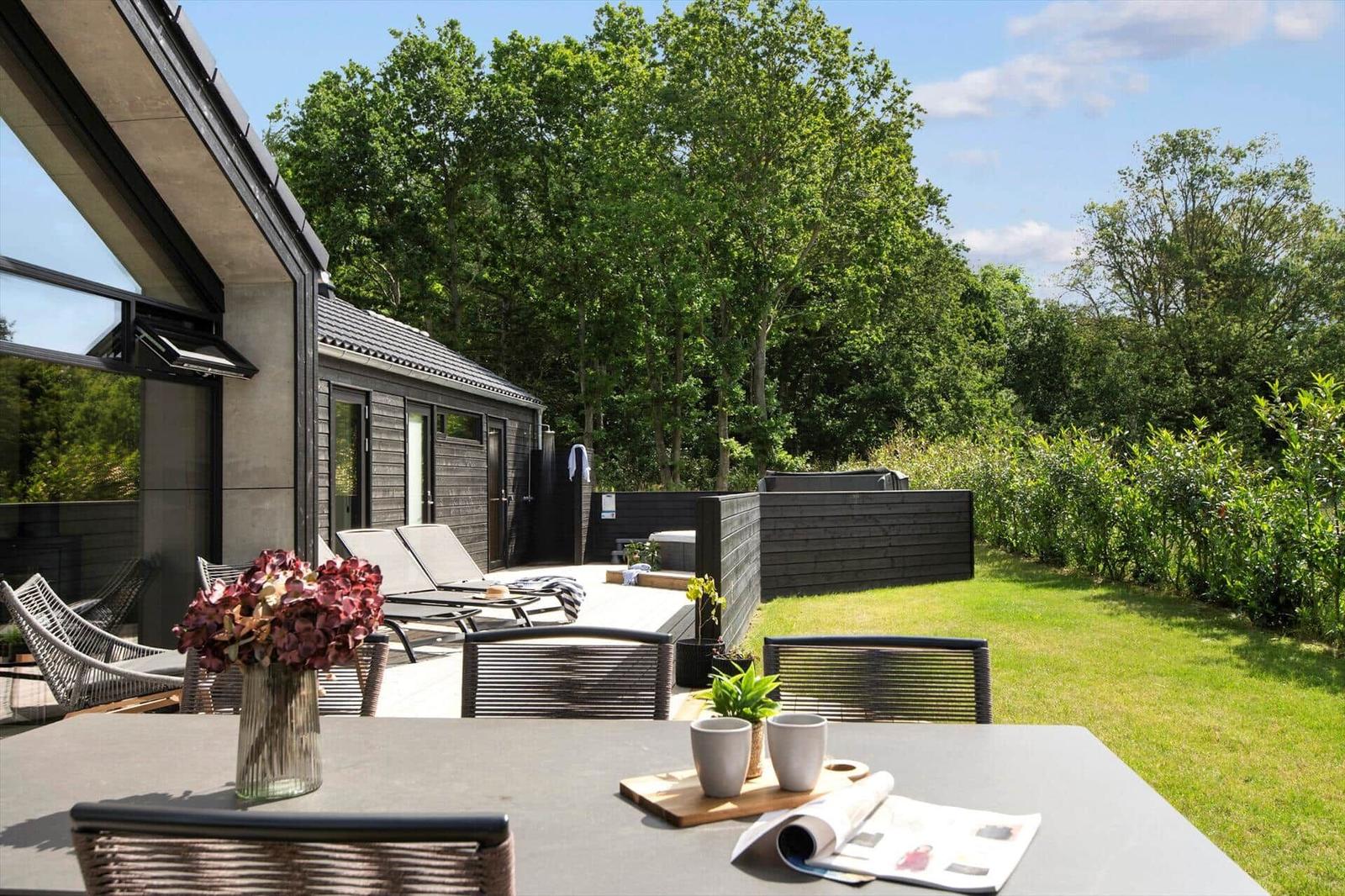 Terrasse mit Tisch, Stühlen und Blumen. Hinterhof mit Liegen und Garten.