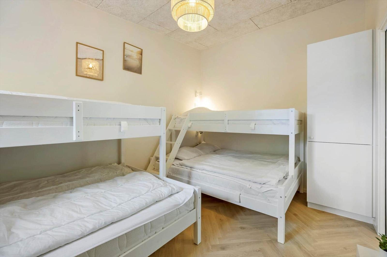 Zwei weiße Etagenbetten mit Matratzen und Bettwäsche. Holzboden und weißer Schrank.