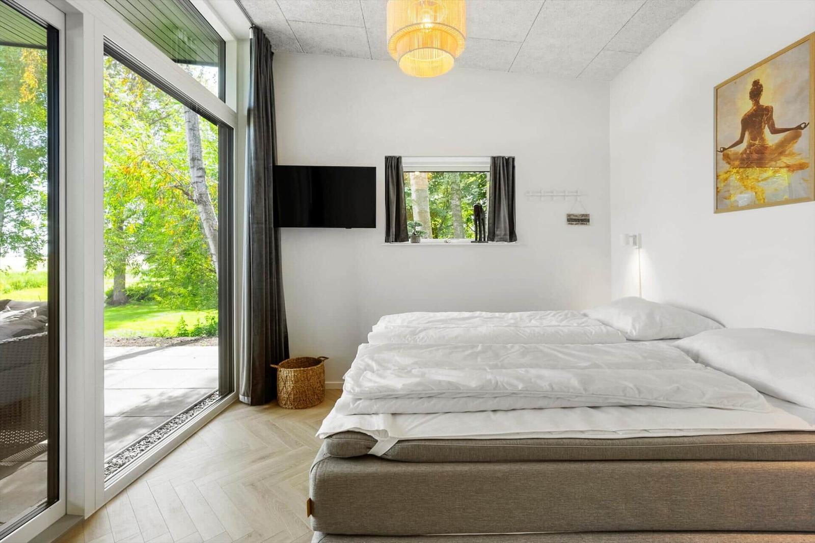 Schlafzimmer mit großem Bett, TV und Blick auf grünen Garten.