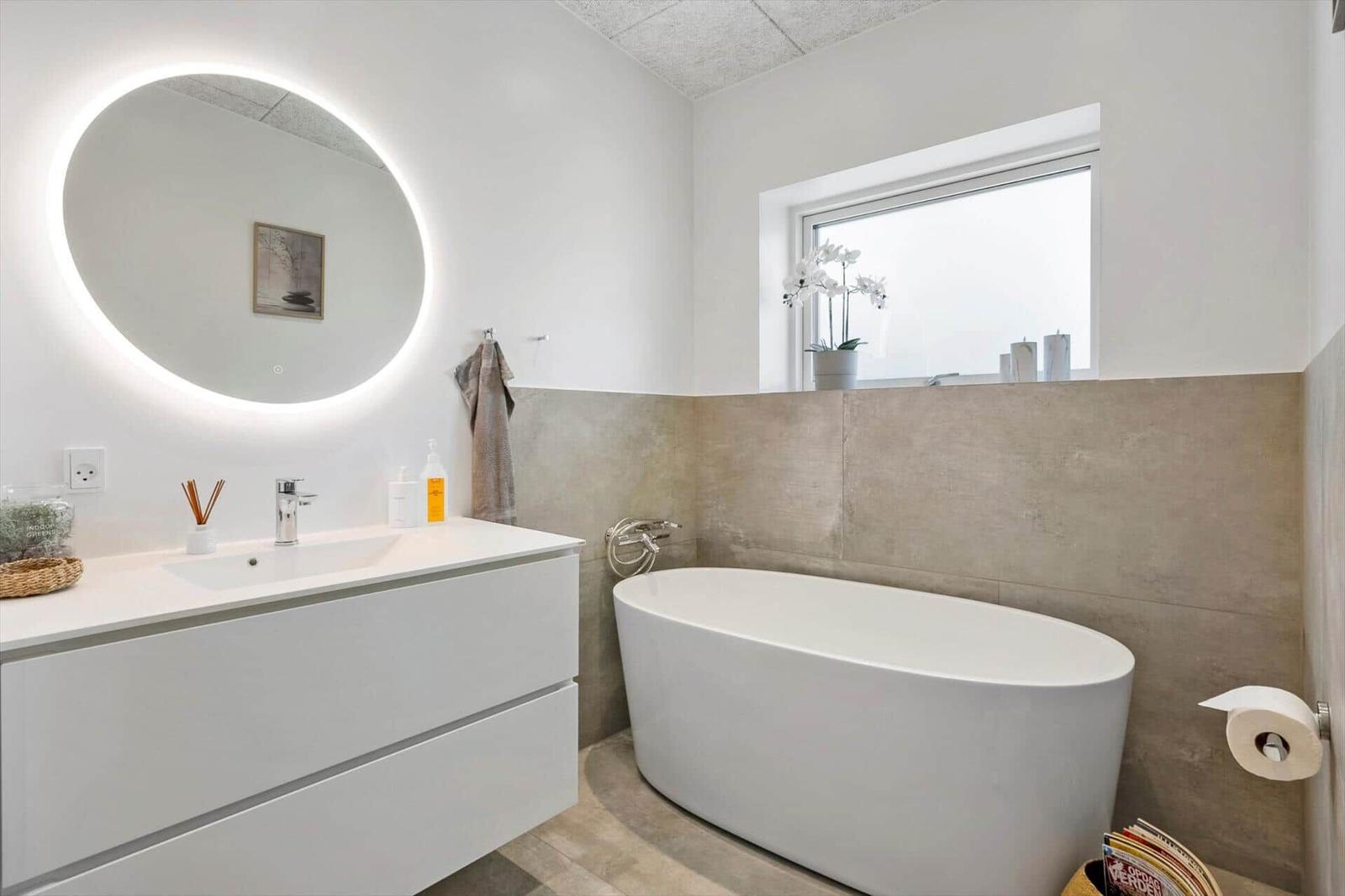 Bad mit freistehender Badewanne, Waschtisch und runden Spiegel mit LED-Beleuchtung.