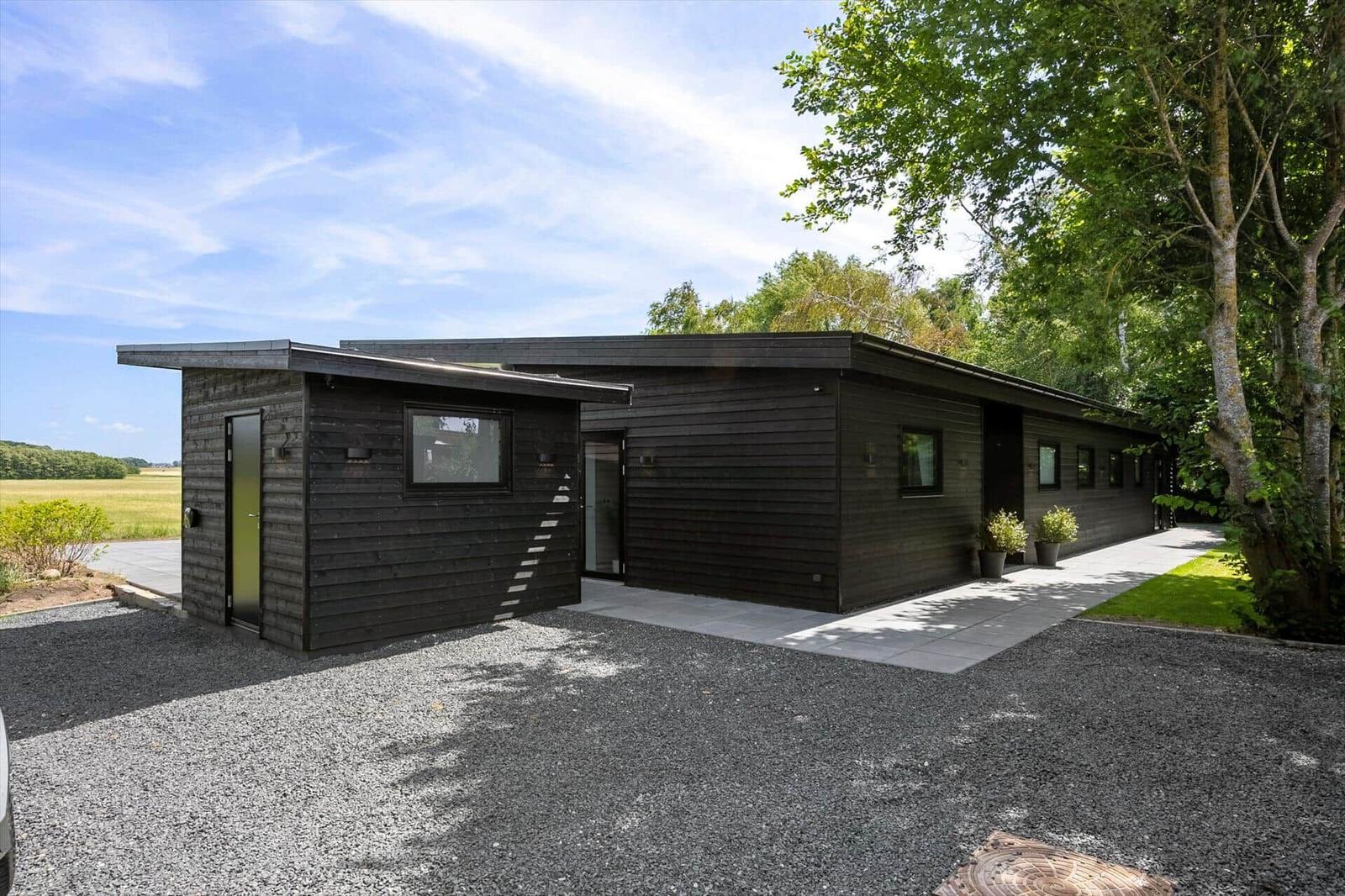 Moderne Holzhütte mit Terrasse, umgeben von Bäumen und Feldern.