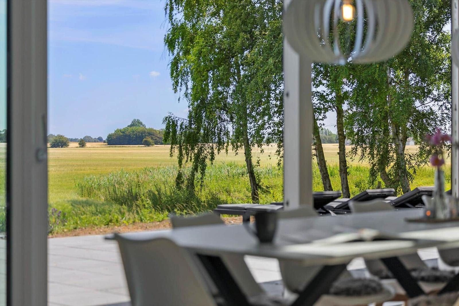 Terrasse mit Tisch und Stühlen. Blick auf grüne Wiesen und Bäume.