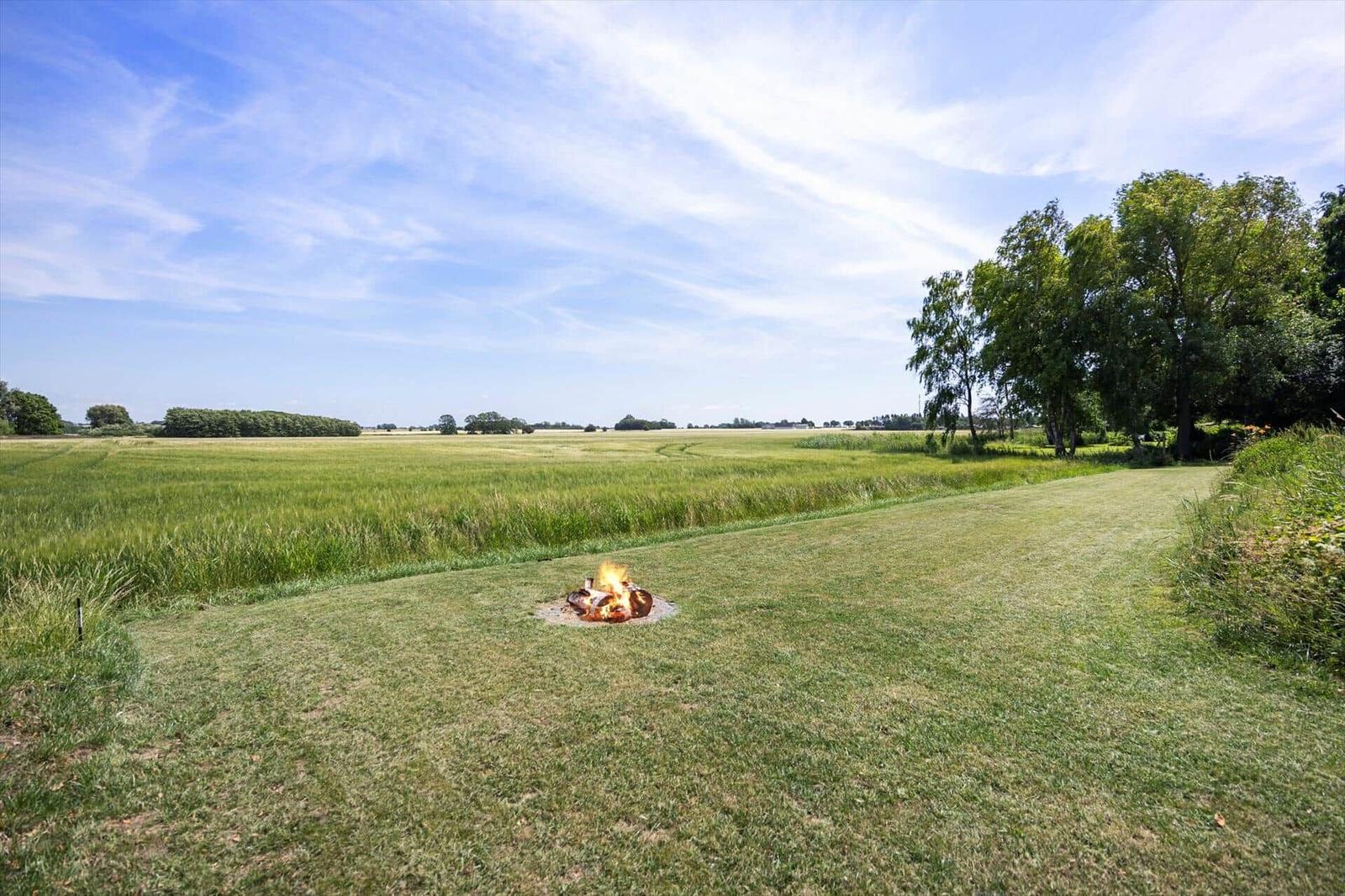 Ein brennender Grill auf einer grünen Wiese mit Blick auf Felder und Bäume.
