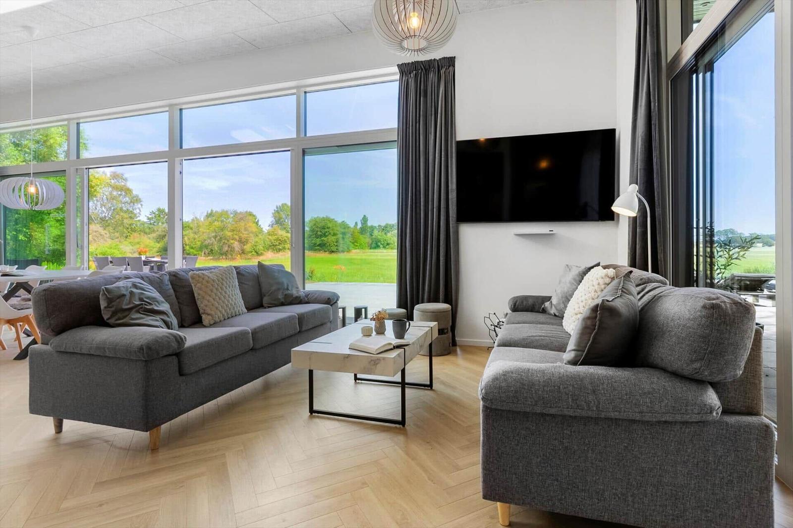 Wohnzimmer mit zwei grauen Sofas, Couchtisch und großen Fenstern zur Aussicht.
