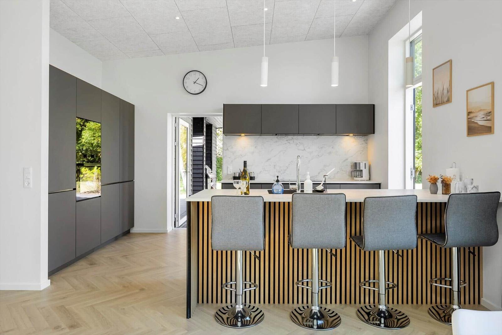 Moderne Küche mit Barhocker und integriertem Kühlschrank. Helle Holzböden und graue Schränke.
