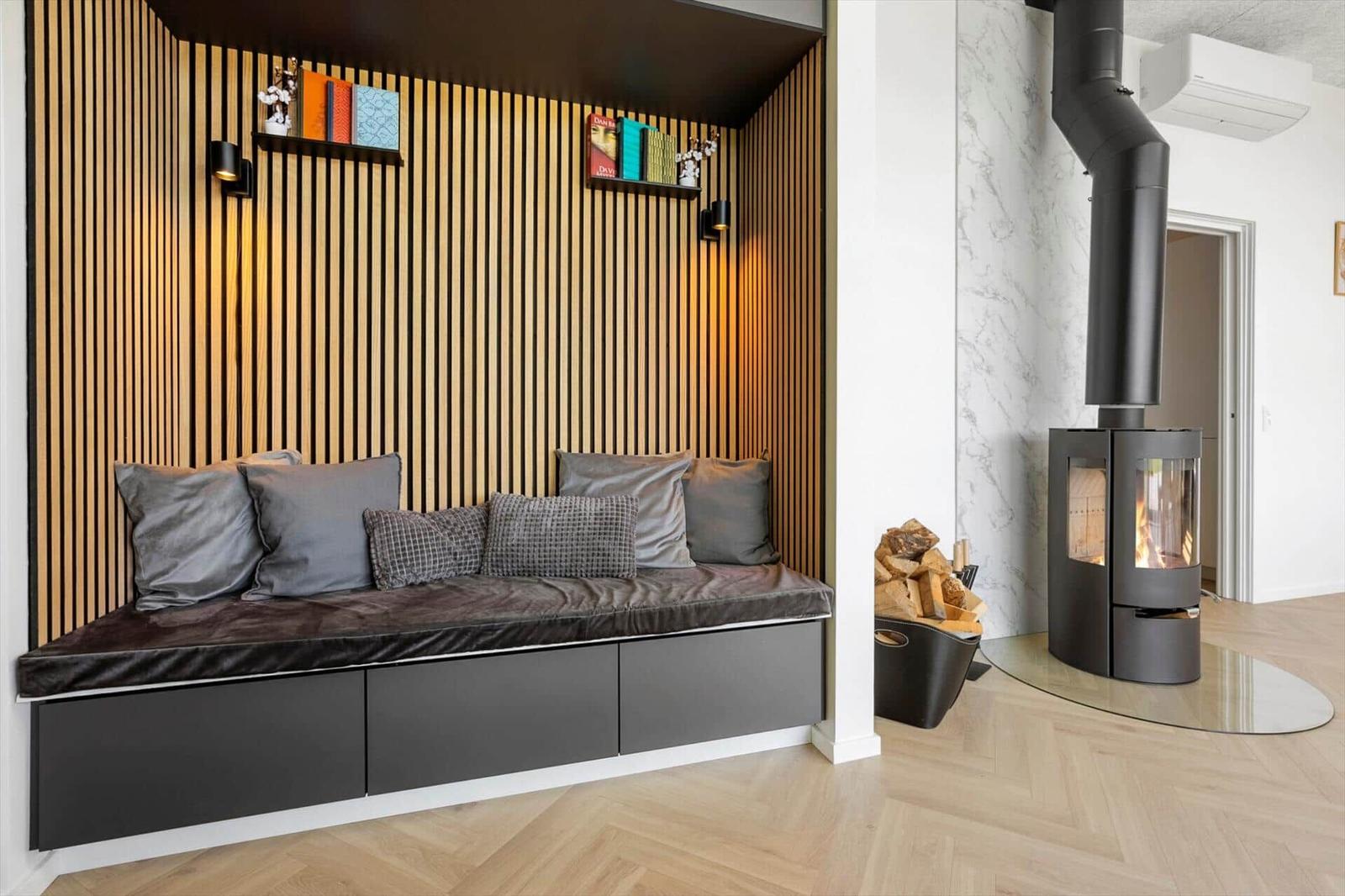 Sitzbank mit Kissen an Holzwand, Kaminofen und Holzstapel