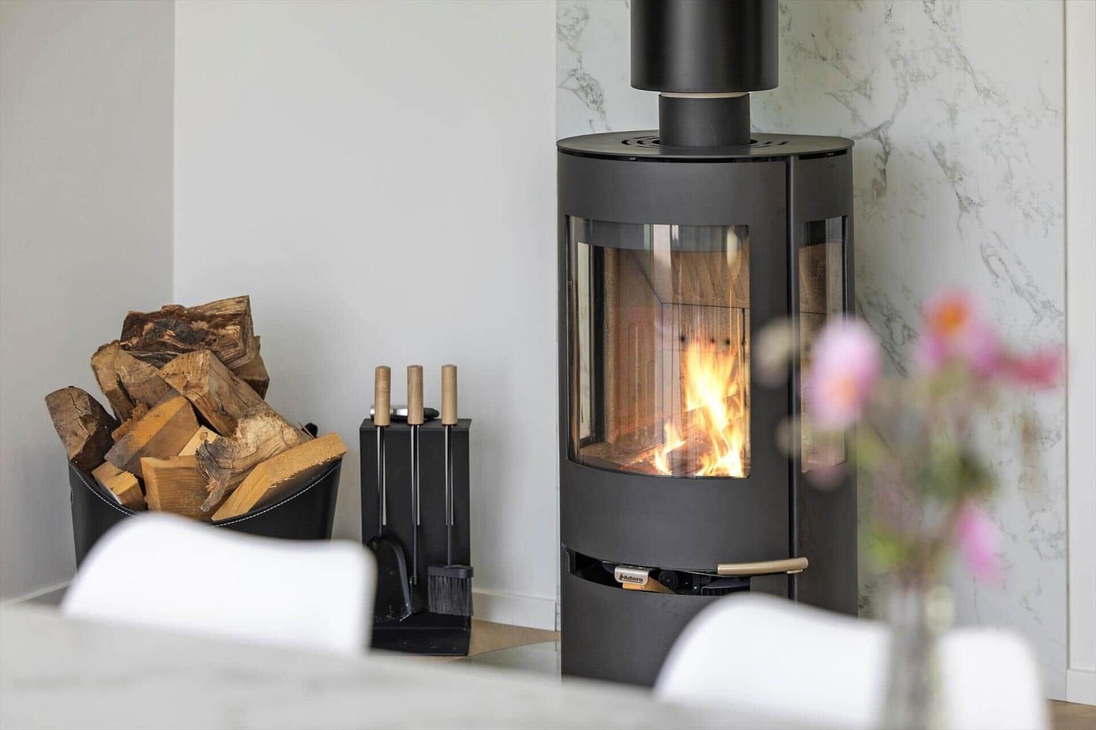 Moderne Holzofen mit brennendem Feuer, daneben Holzstapel und Feuerzeugset.