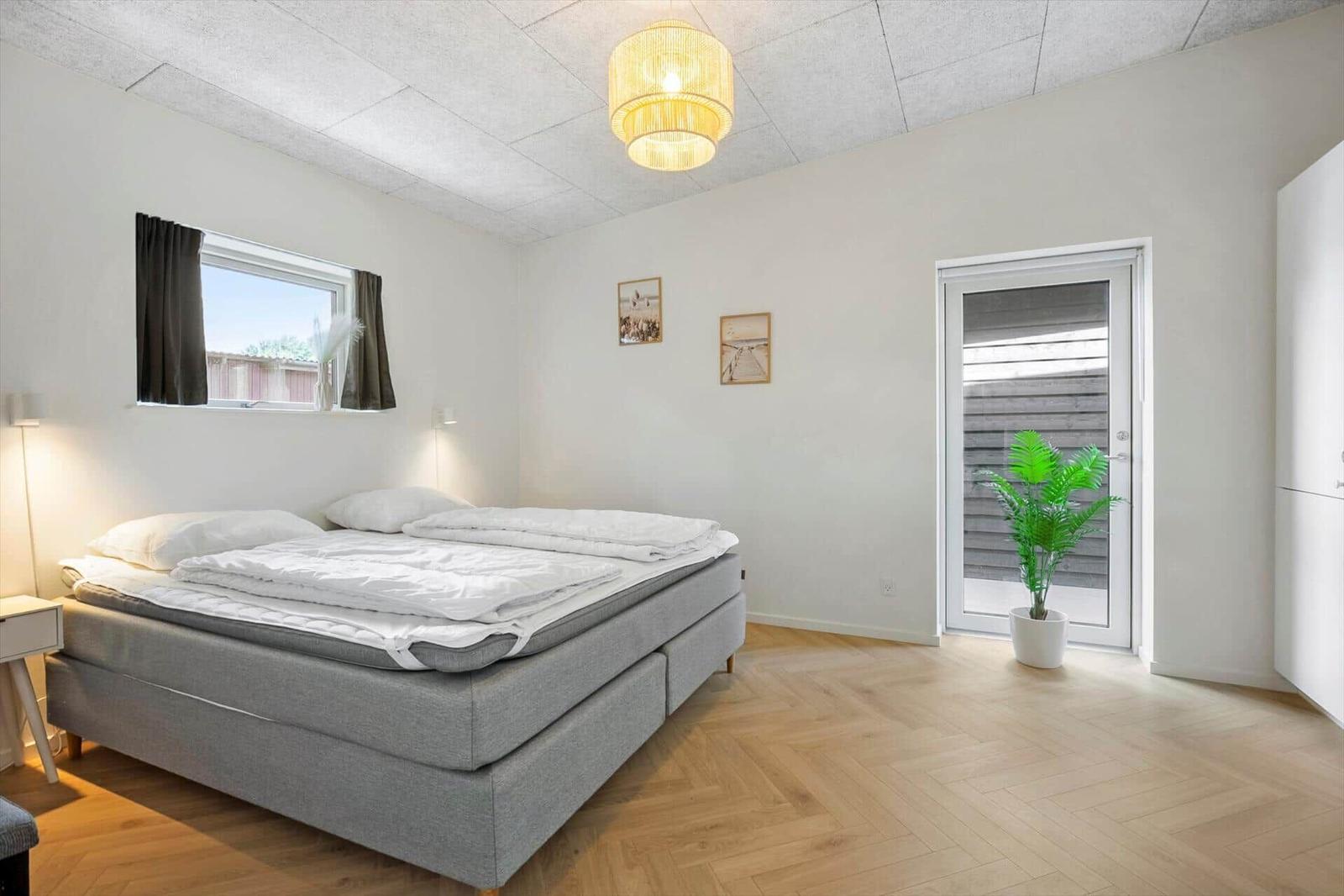 Schlafzimmer mit Bett, Fenster, Tür und Pflanze.