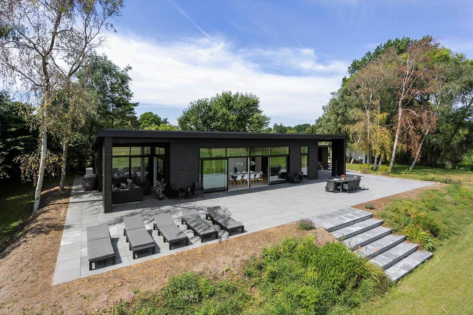 Moderne Villa mit großem Außenbereich, Sonnenliegen und Blick auf Bäume.
