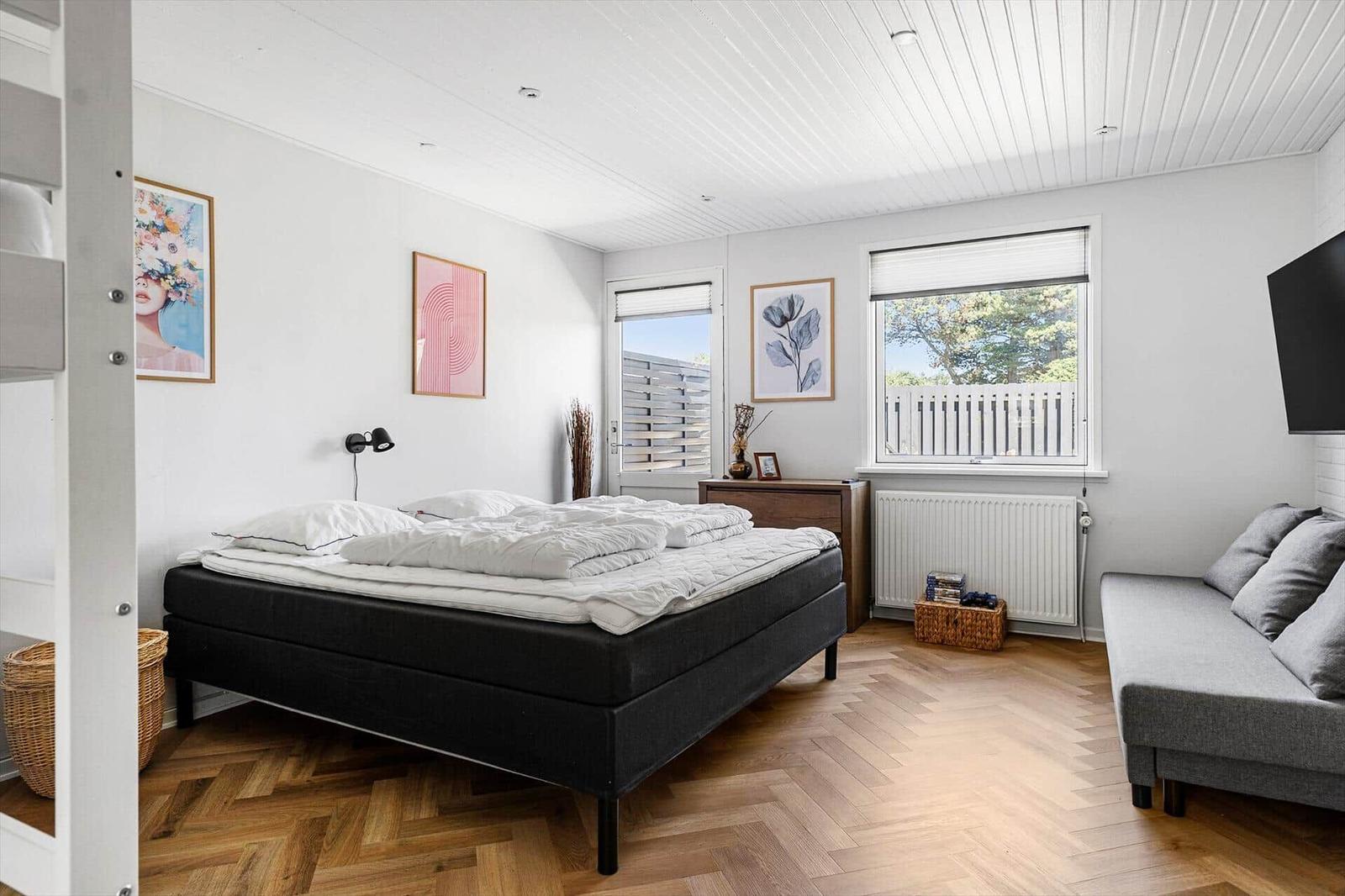 Bedroom with bed, sofa, and windows. Wooden floor and wall art.