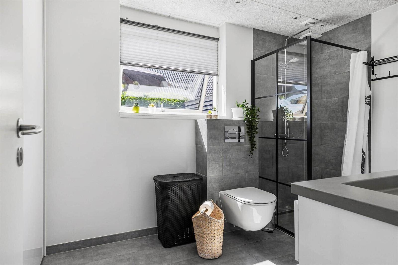 Bathroom with shower, toilet, and window with view outside.