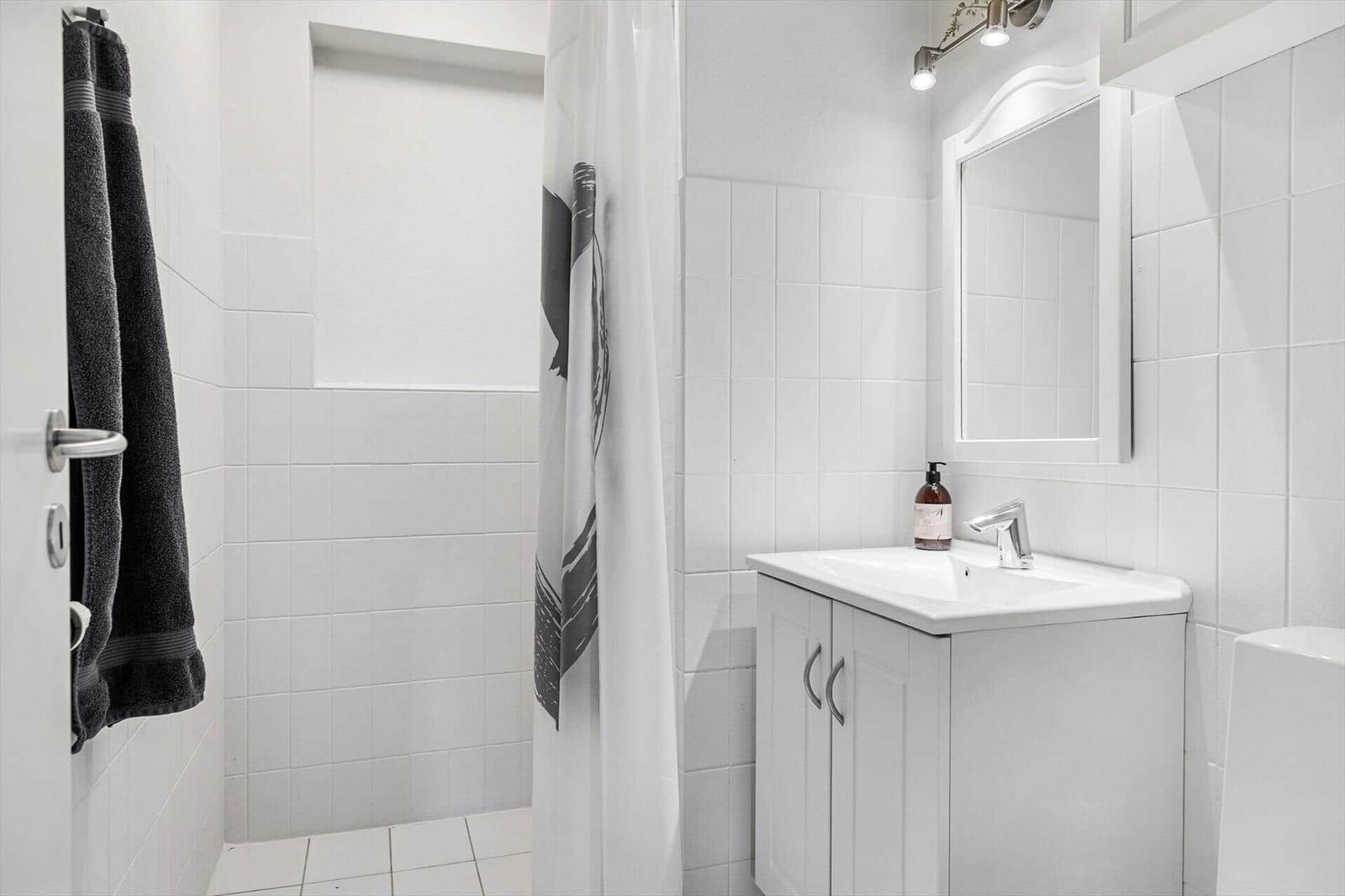 Bathroom with shower, sink, and mirror. White tiles and towel rack.