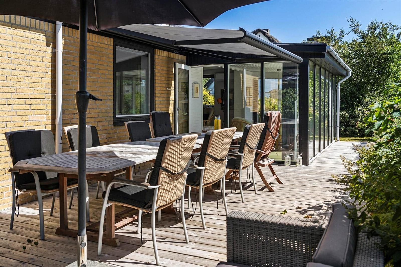 Deck with table, chairs, and sun cover. Glass wall leads into the house.
