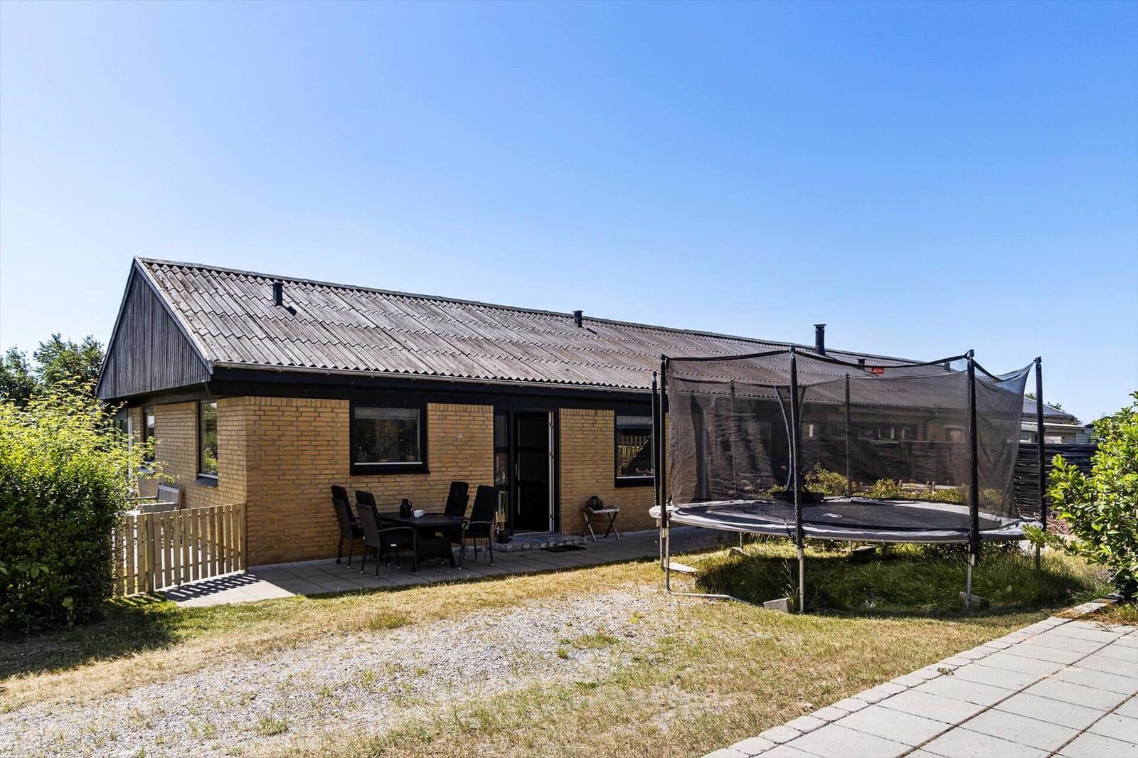 A house with a terrace, table, chairs, and trampoline in the garden.