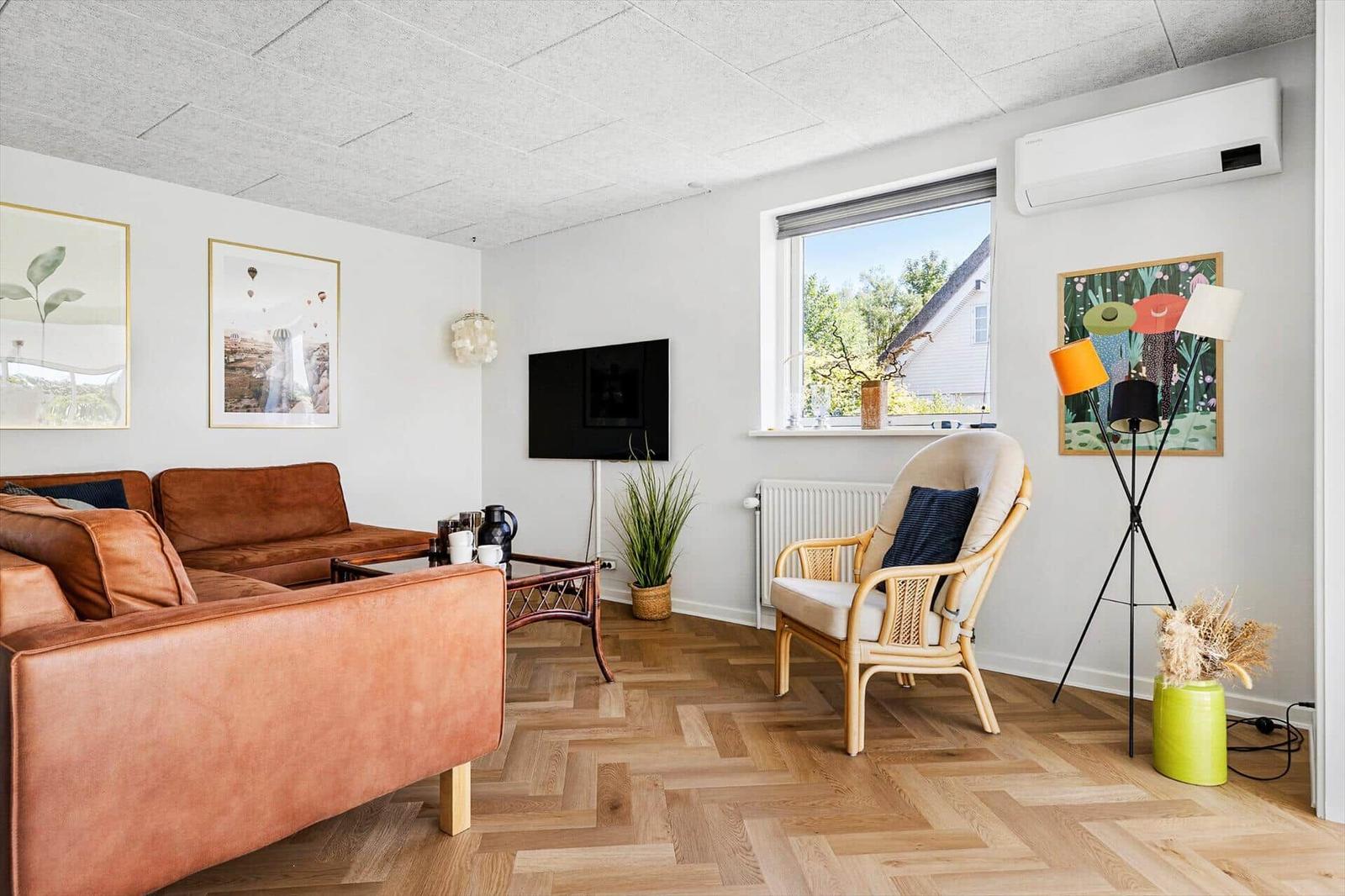 Living room with brown sofa, wooden floor, and window. Wall art and floor lamp visible.
