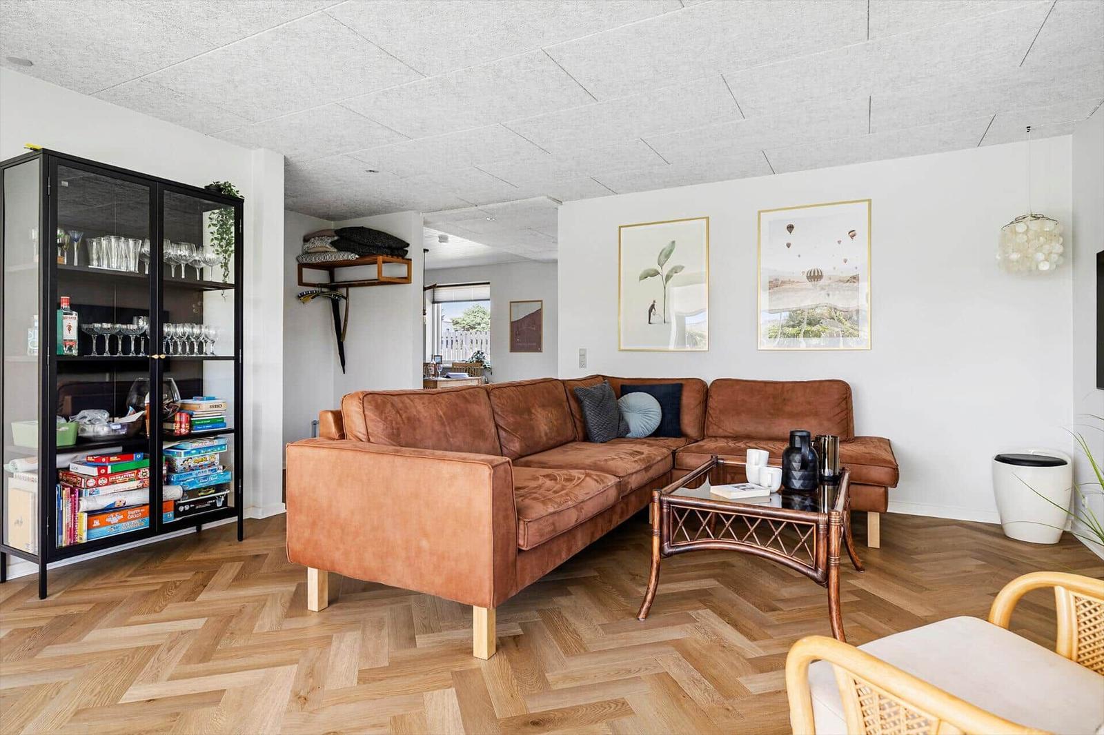 A living room with brown sofa, wooden floor, and glass cabinet.