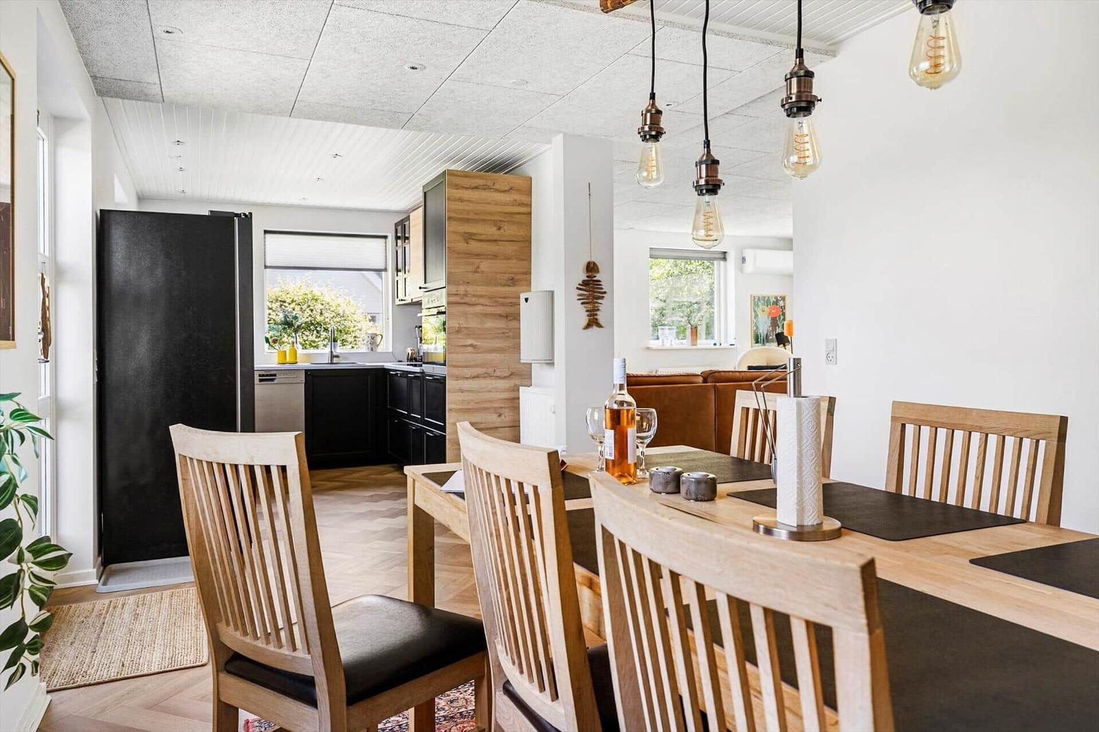 Dining area with wooden table and chairs. Kitchen with black cabinets and window.