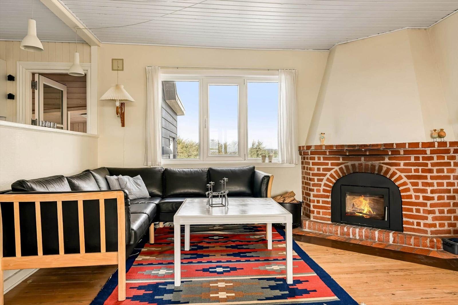 Wohnzimmer mit Sofa, Kamin und Fenster mit Blick nach draußen.