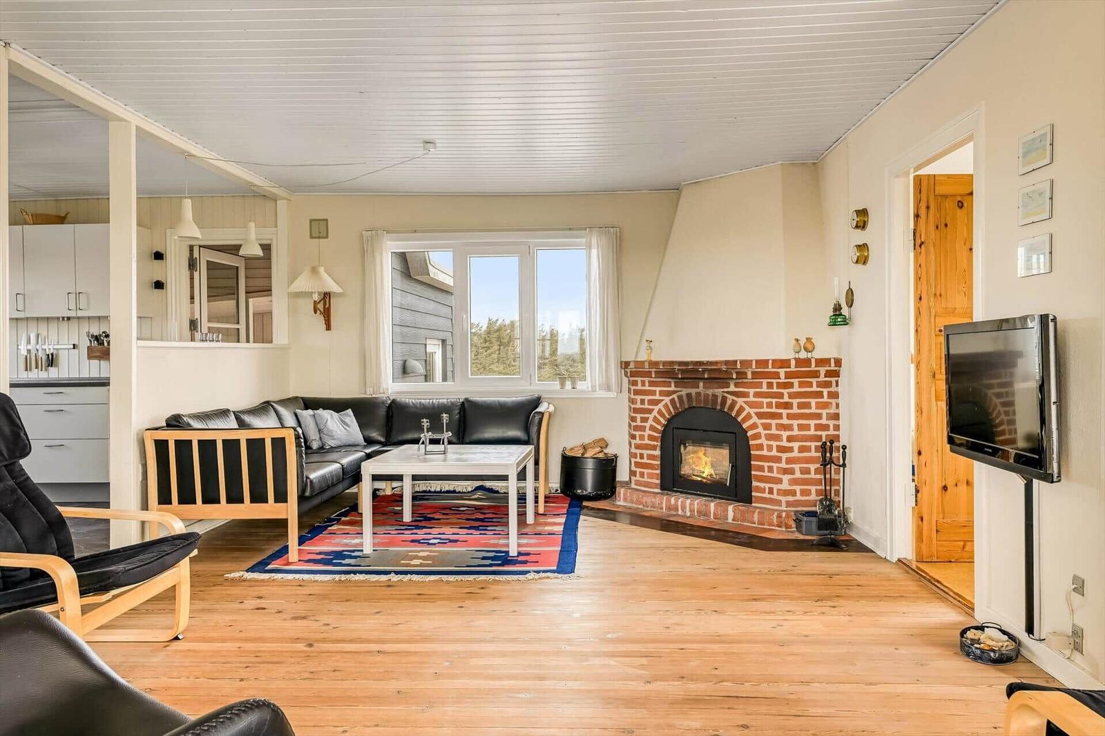 Wohnzimmer mit Kamin, Sofa, TV und Holzboden. Küche im Hintergrund sichtbar.
