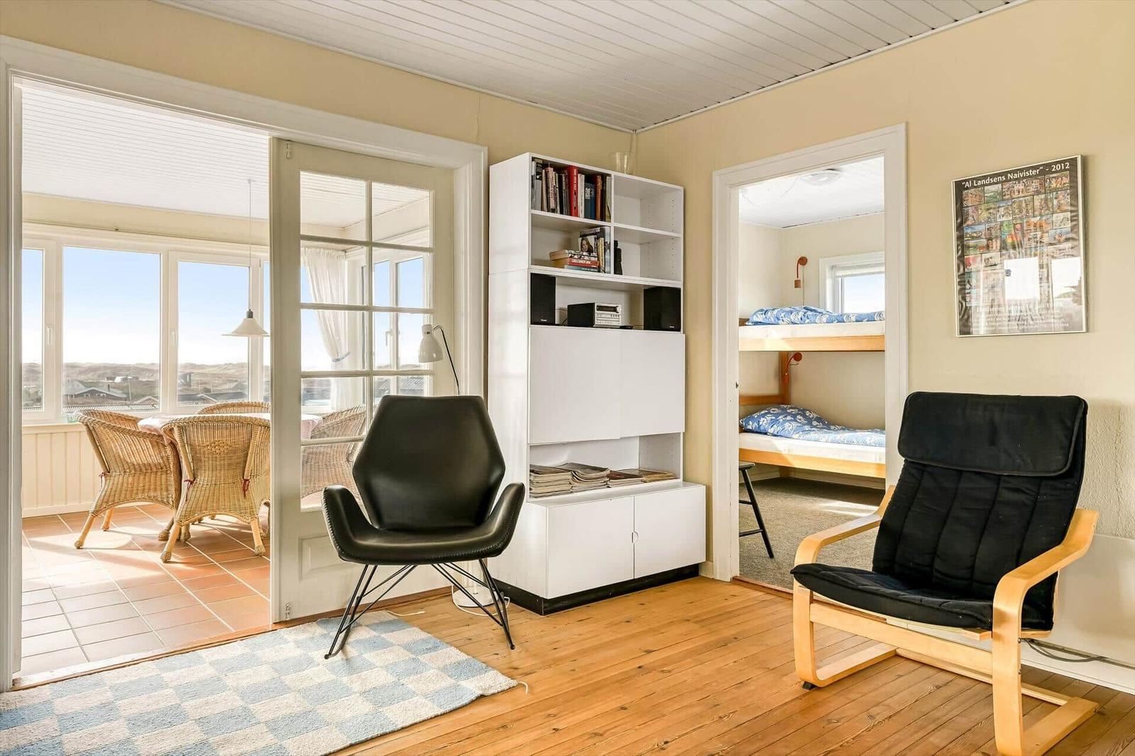 Zimmer mit zwei schwarzen Sesseln, Bücherregal und Blick auf Essbereich mit Terrasse.