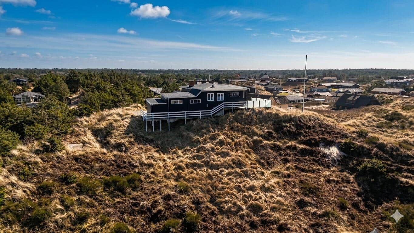 Schwarzes Haus auf Dünen mit weißer Veranda und Blick auf Wald und Ferienorte.