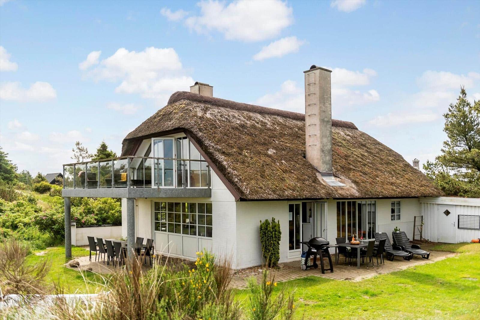 Haus mit Strohdach, Terrasse und Gartenbereich mit Grill und Liegestühlen.