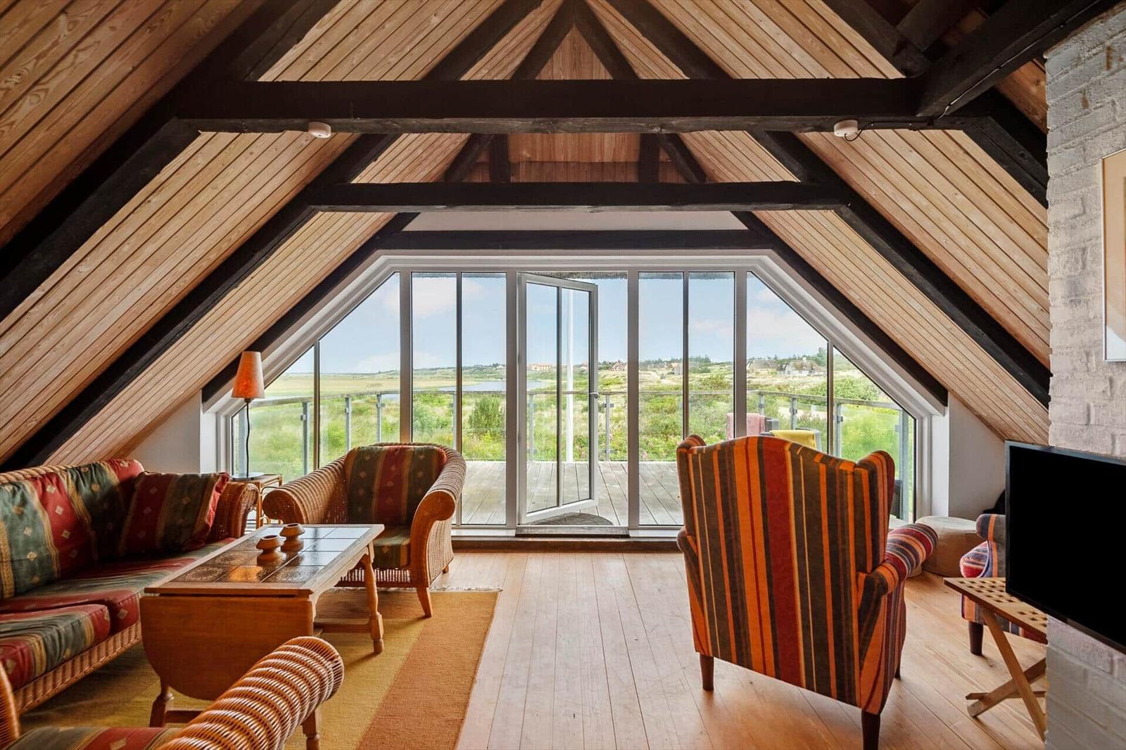 Wohnzimmer mit Holzdecke, Sitzmöbel und Blick auf Terrasse und Landschaft.