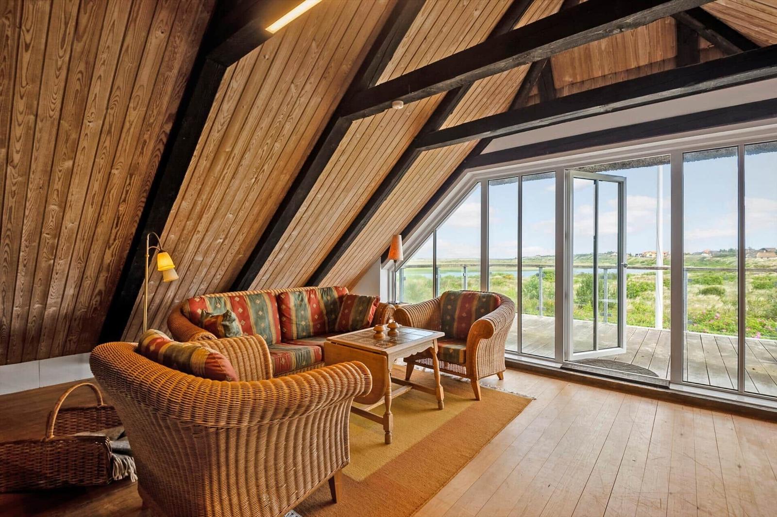 Wohnraum mit Sitzgelegenheiten, Holzdecke und Blick auf Terrasse und Landschaft.