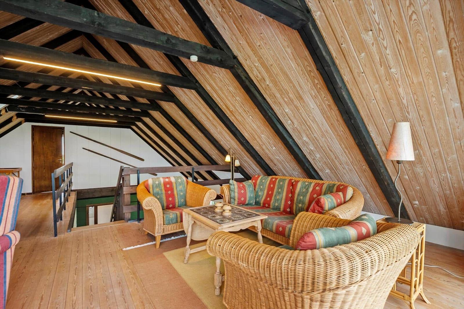 Wohnbereich mit Rattanmöbeln und Holzdecke. Couch und Sessel mit bunten Kissen.