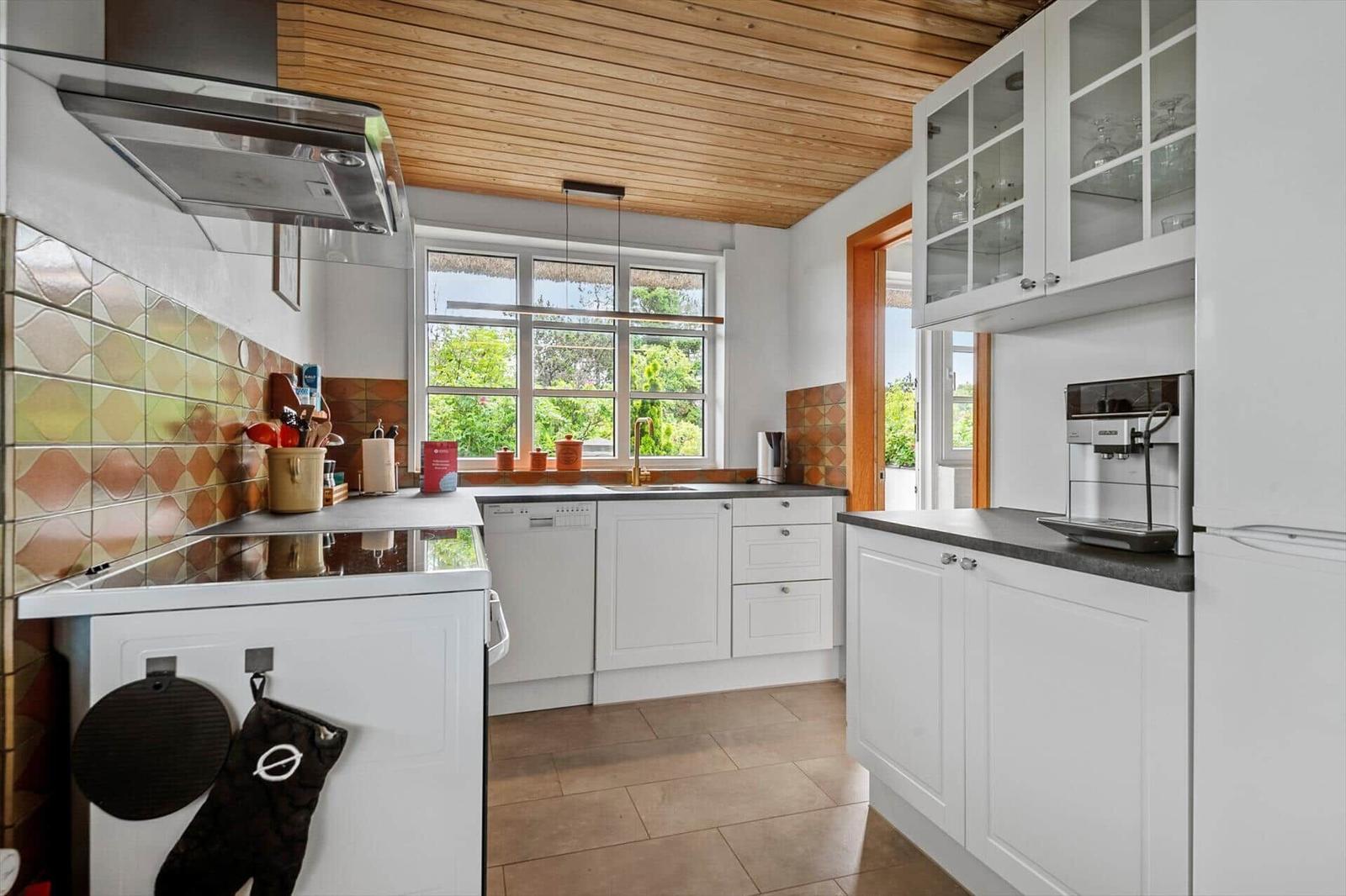 Küche mit weißen Schränken, Holzdecke und Fenster zum Garten.
