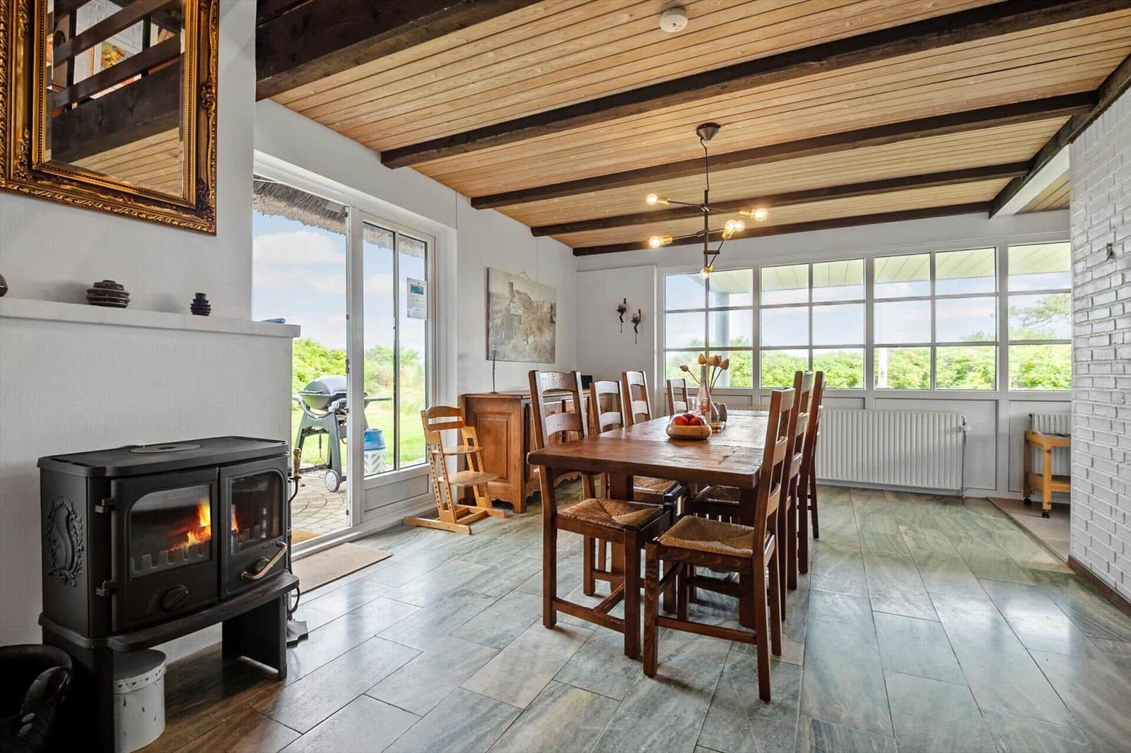 Esszimmer mit Holztisch, Stühlen und Kaminofen. Holzdecke und große Fenster.
