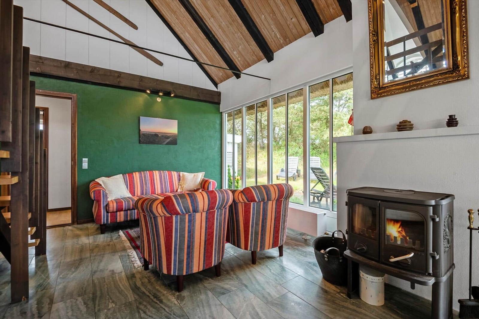 Wohnzimmer mit Streifensofa, Kamin und großem Fensterblick auf den Garten.