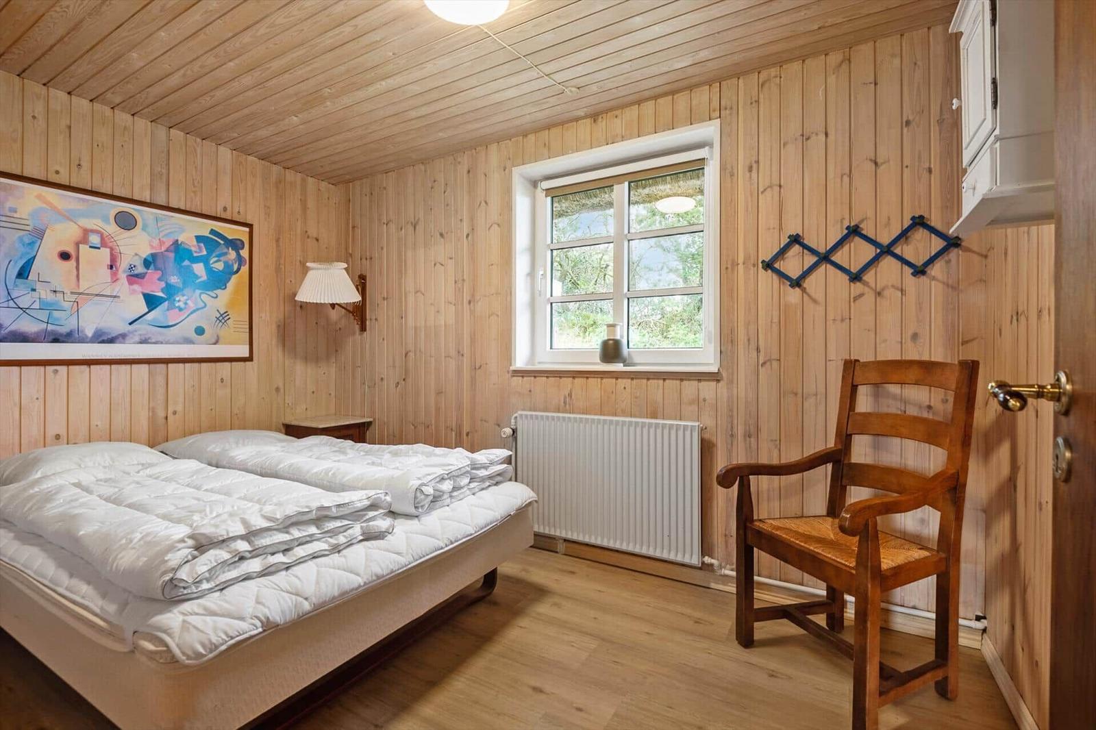 Schlafzimmer mit Holzwand, Bett, Stuhl und Fenster.