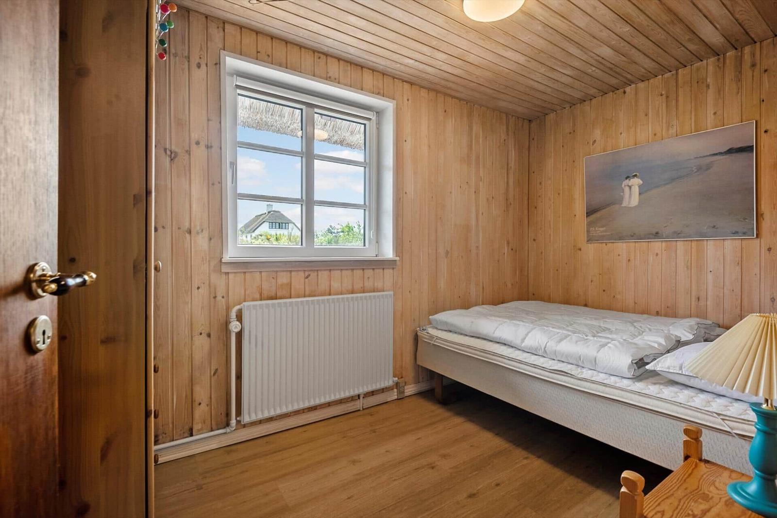 Schlafzimmer mit Holzwand, Bett, Fenster und Gemälde an der Wand.