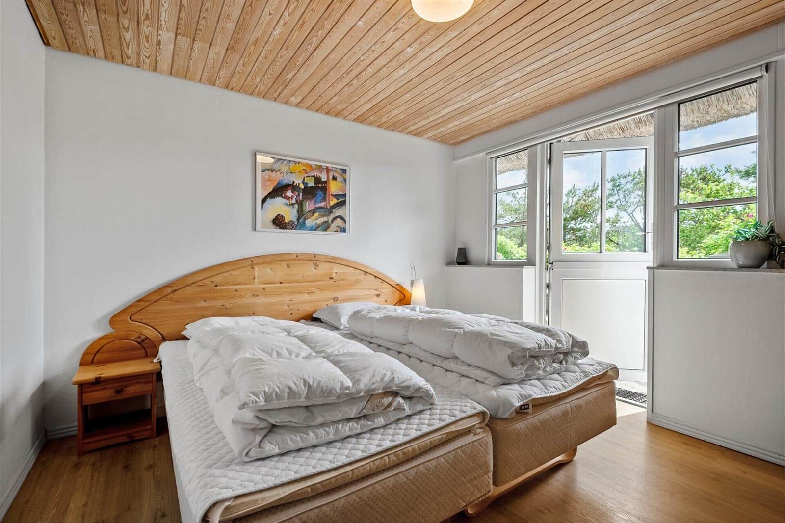 Schlafzimmer mit Holzboden, Holzdecke und Bett mit weißen Bettwäsche.
