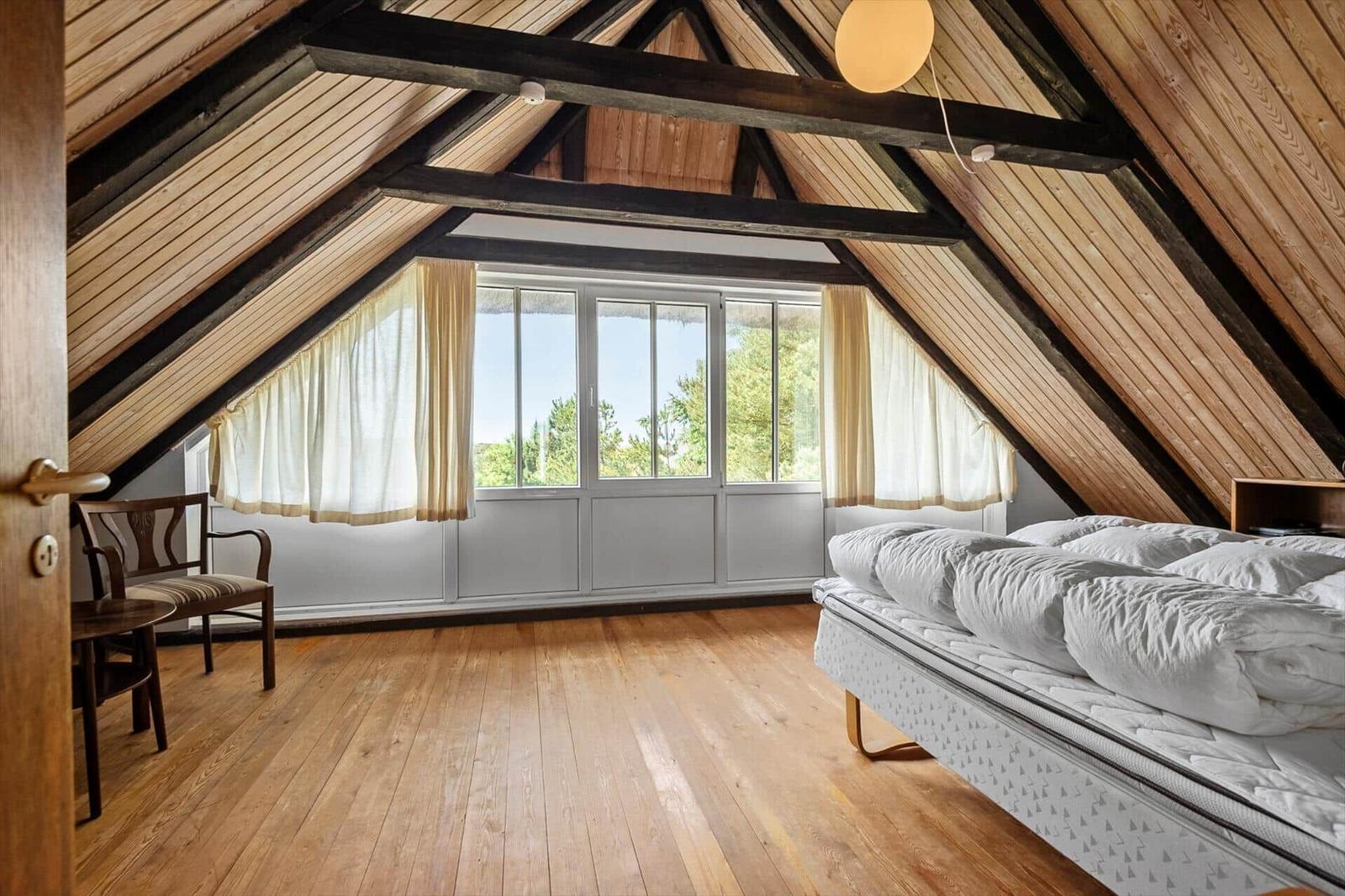 Schlafzimmer mit Holzdecke, großem Fenster und Bett.