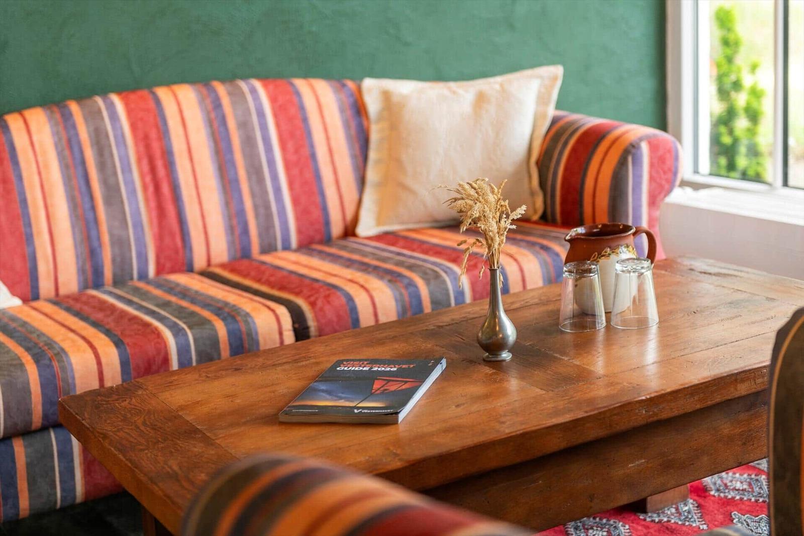 Ein Sofa mit Streifenmuster steht vor einem grünen Wand. Auf dem Tisch liegen ein Buch und ein Vasen.