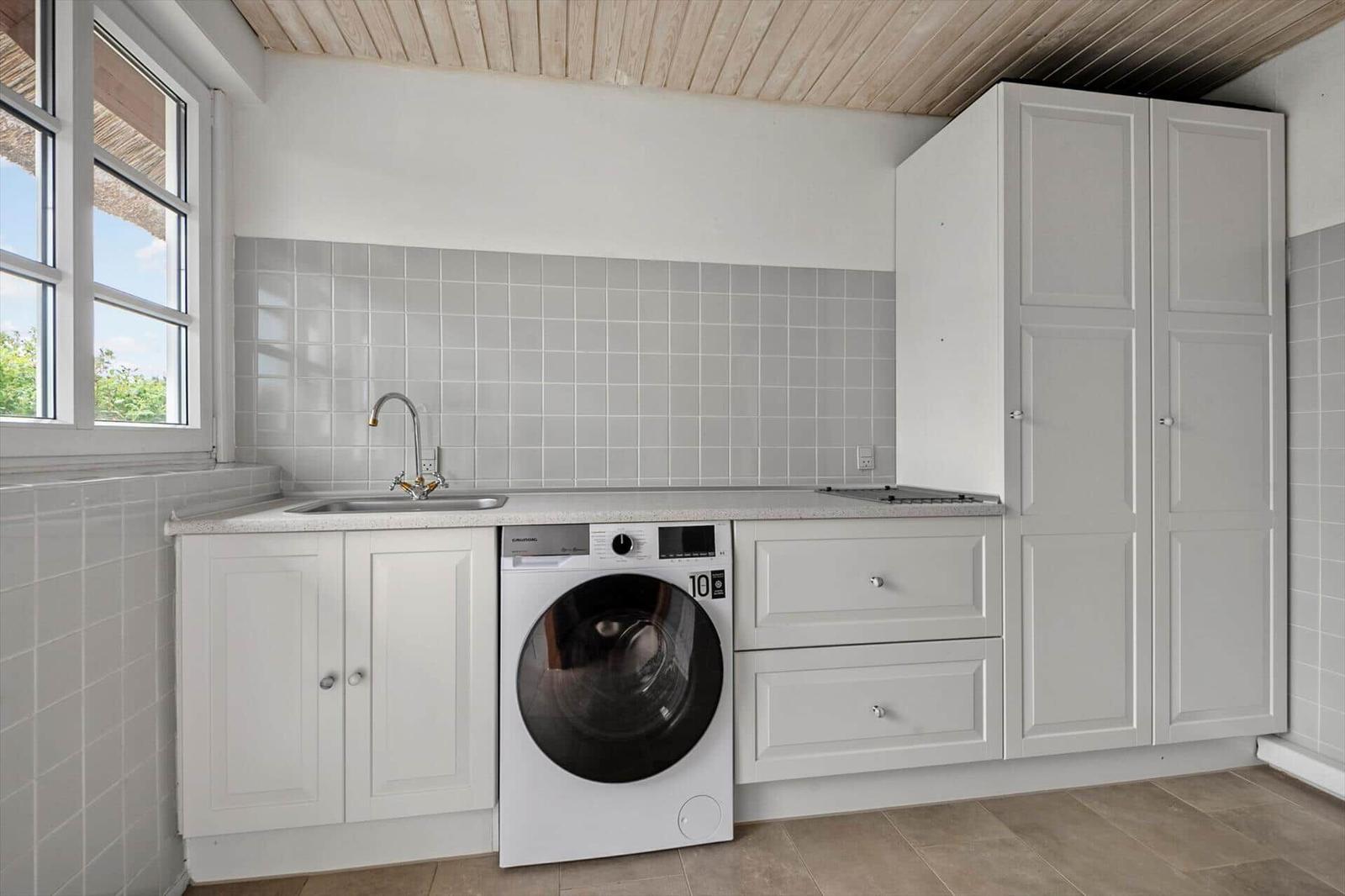 Küche mit Waschmaschine, Spüle und weißen Schränken unter Dachschrägen.